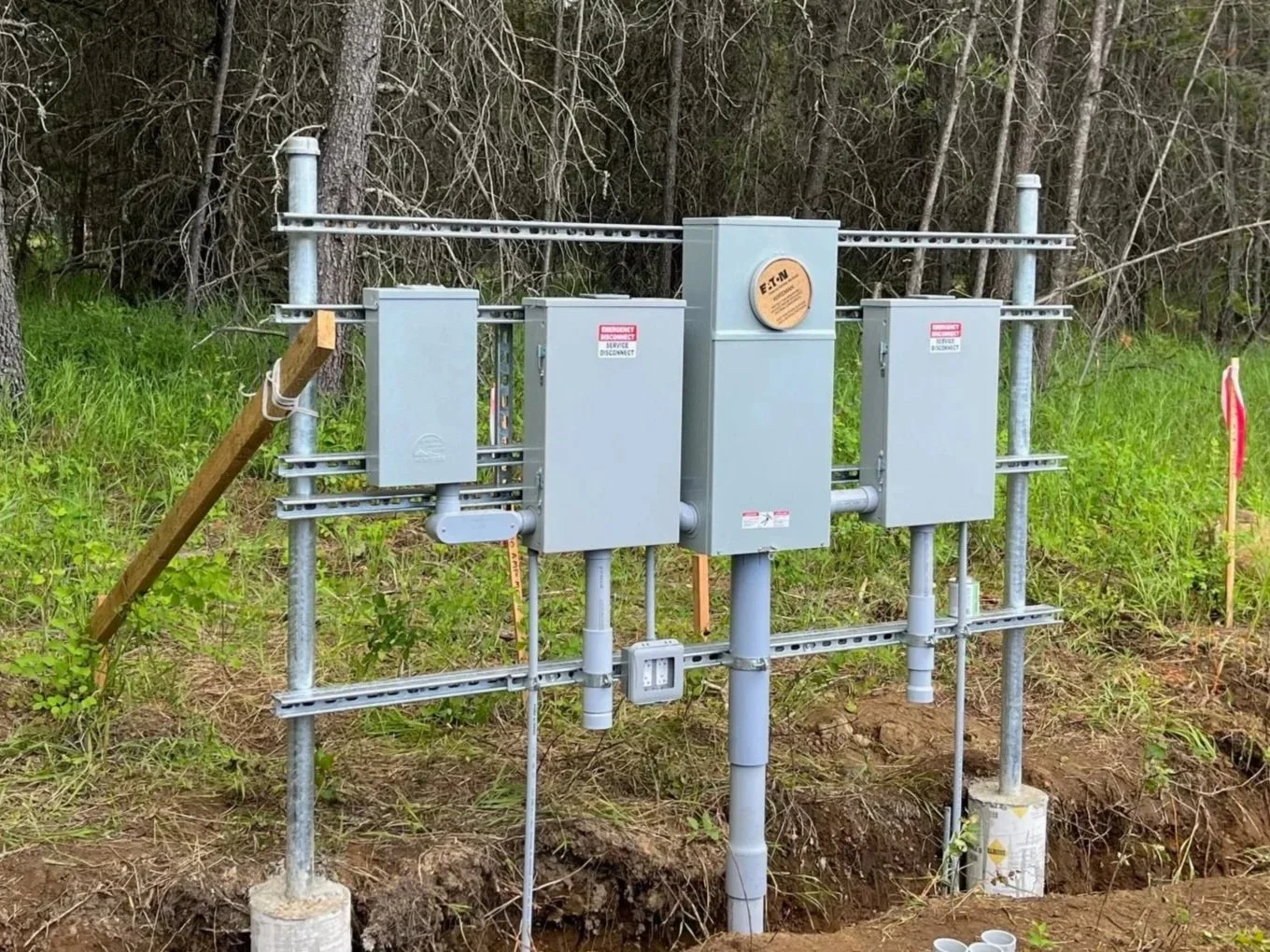 Electrical utility box and conduit installed in a grassy, wooded area with trees in the background.