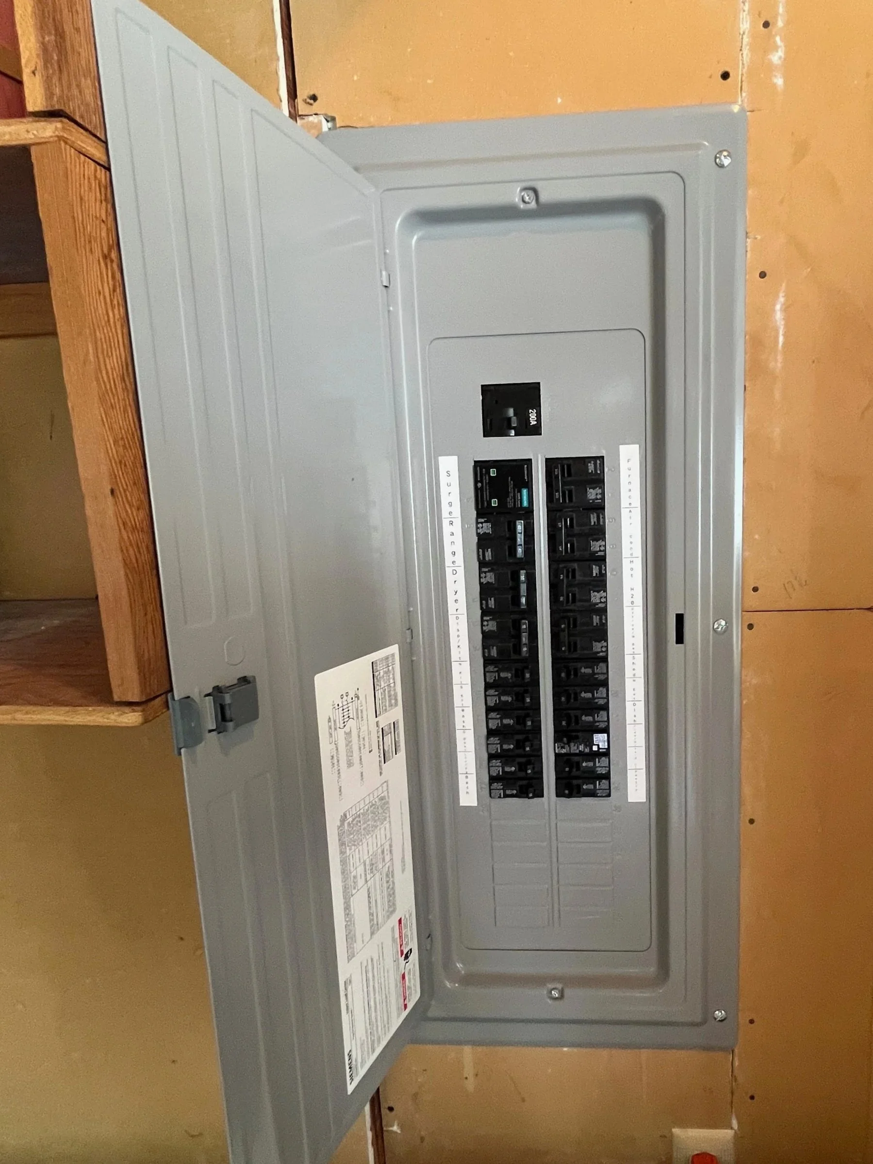 Gray electrical breaker panel mounted on a wall with various switches inside.