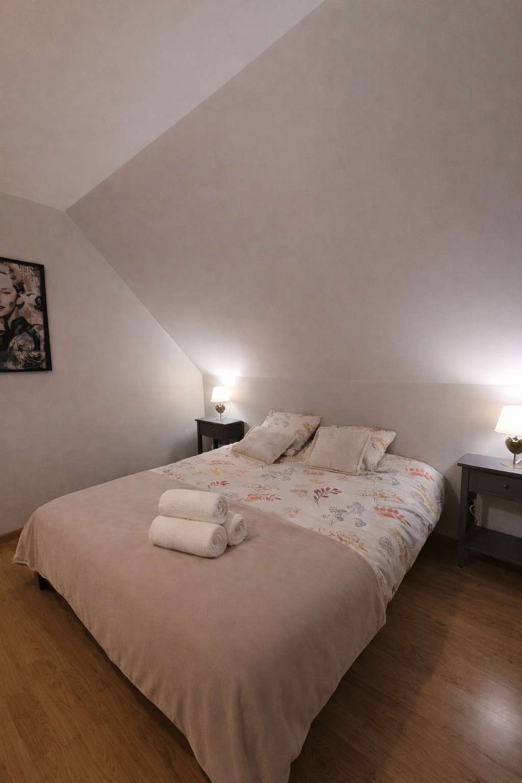 Chambre à coucher avec lit double, trois serviettes pliées sur le lit, deux tables de nuit avec lampes, et un tableau de Marilyn Monroe sur le mur.