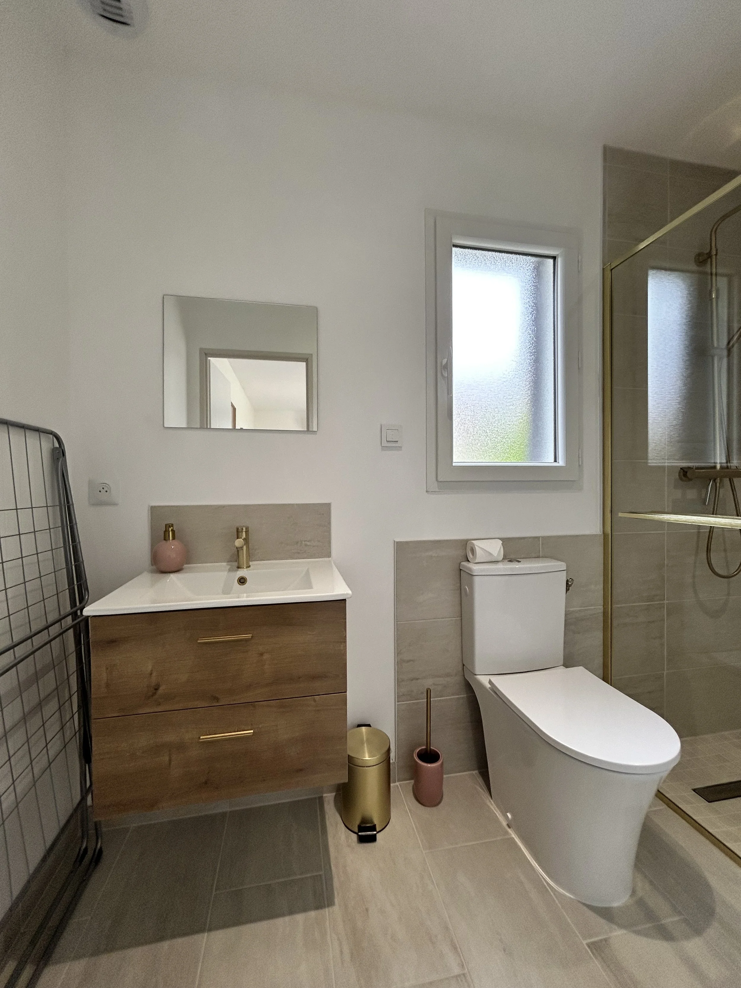 Salle de bain moderne avec un lavabo en bois, un miroir, une fenêtre, un WC blanc, une cabine de douche avec porte en verre, et des accessoires de décoration