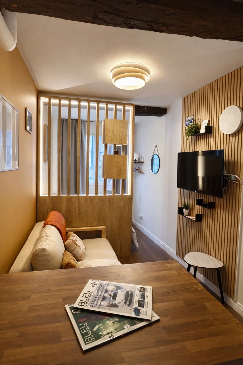 Salon avec canapé beige, table en bois, téléviseur sur un mur en bois, décoration moderne, lampes et plantes.