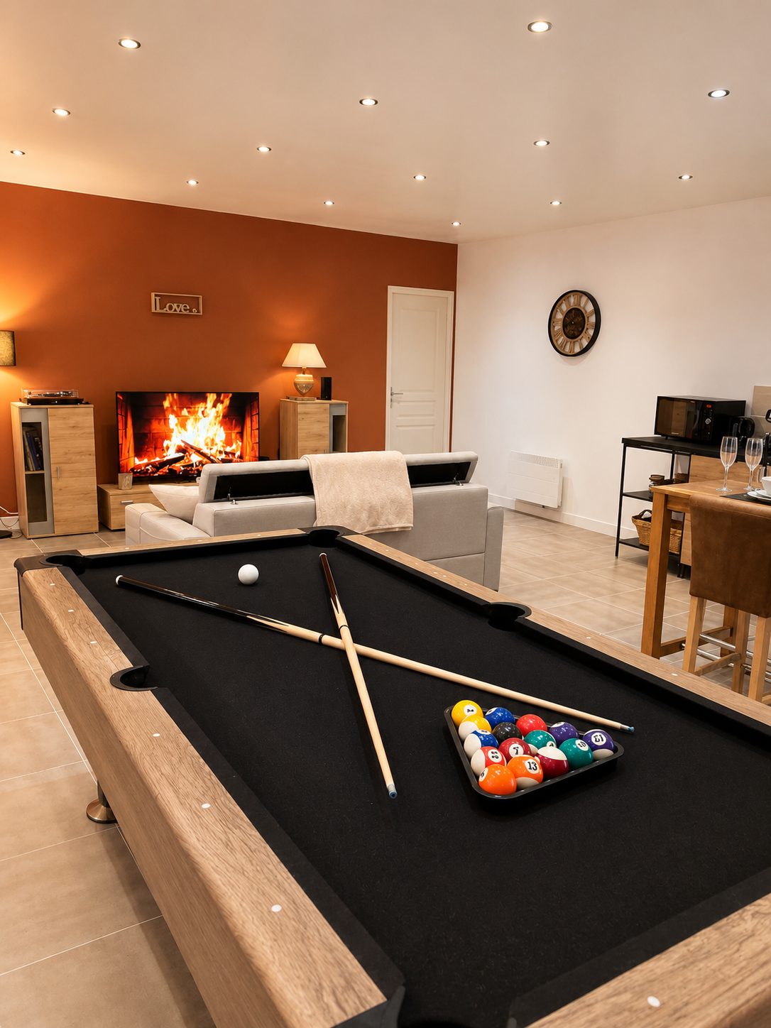 Salle de jeux avec table de billard, canapé, cheminée et télévision dans un salon.