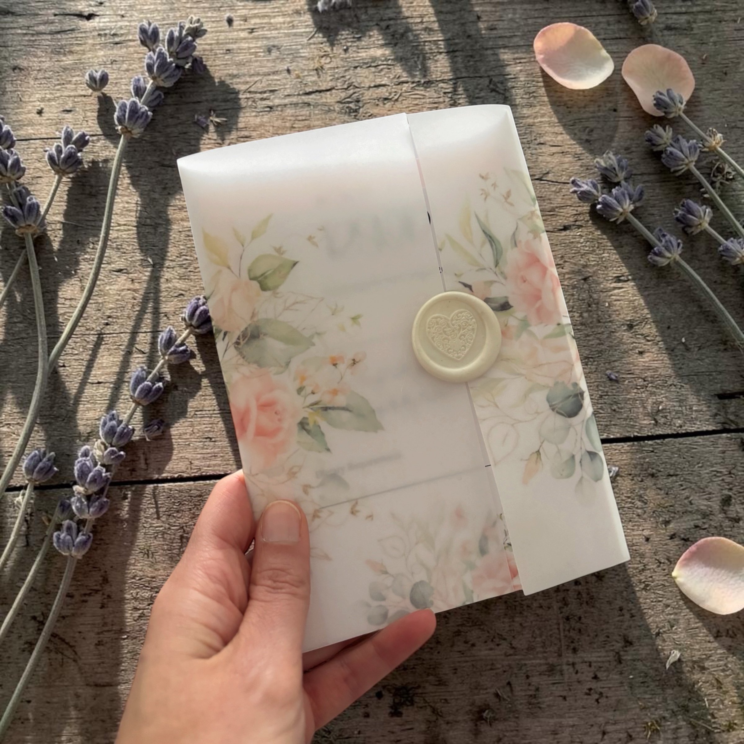 Hand holding a floral-patterned card over a wooden surface with lavender flowers and fallen rose petals.