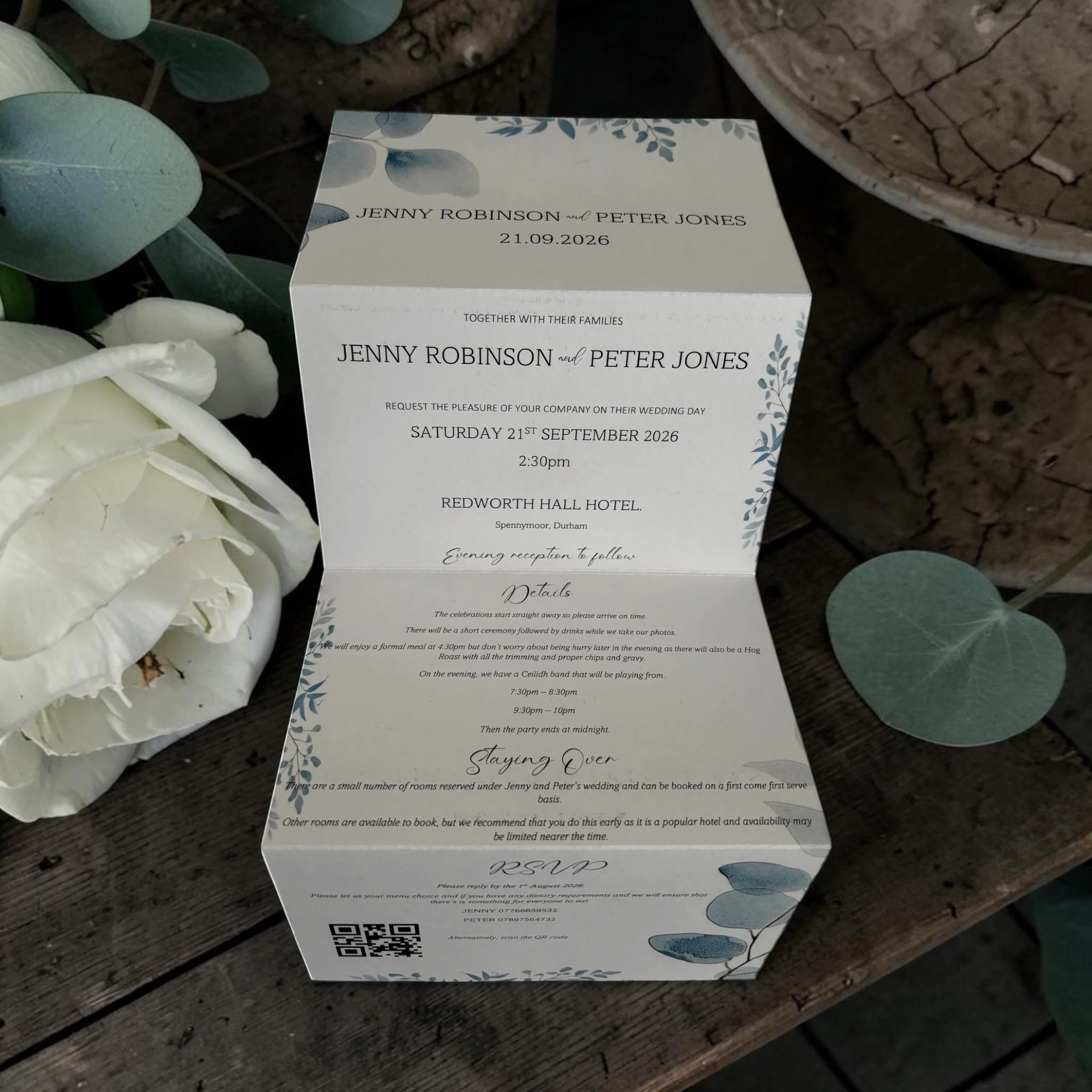 Wedding invitation card on a wooden surface, decorated with botanical illustrations, details for the wedding of Jenny Robinson and Peter Jones scheduled for September 21, 2026, at Redworth Hall Hotel in Durham, including timings and event information.