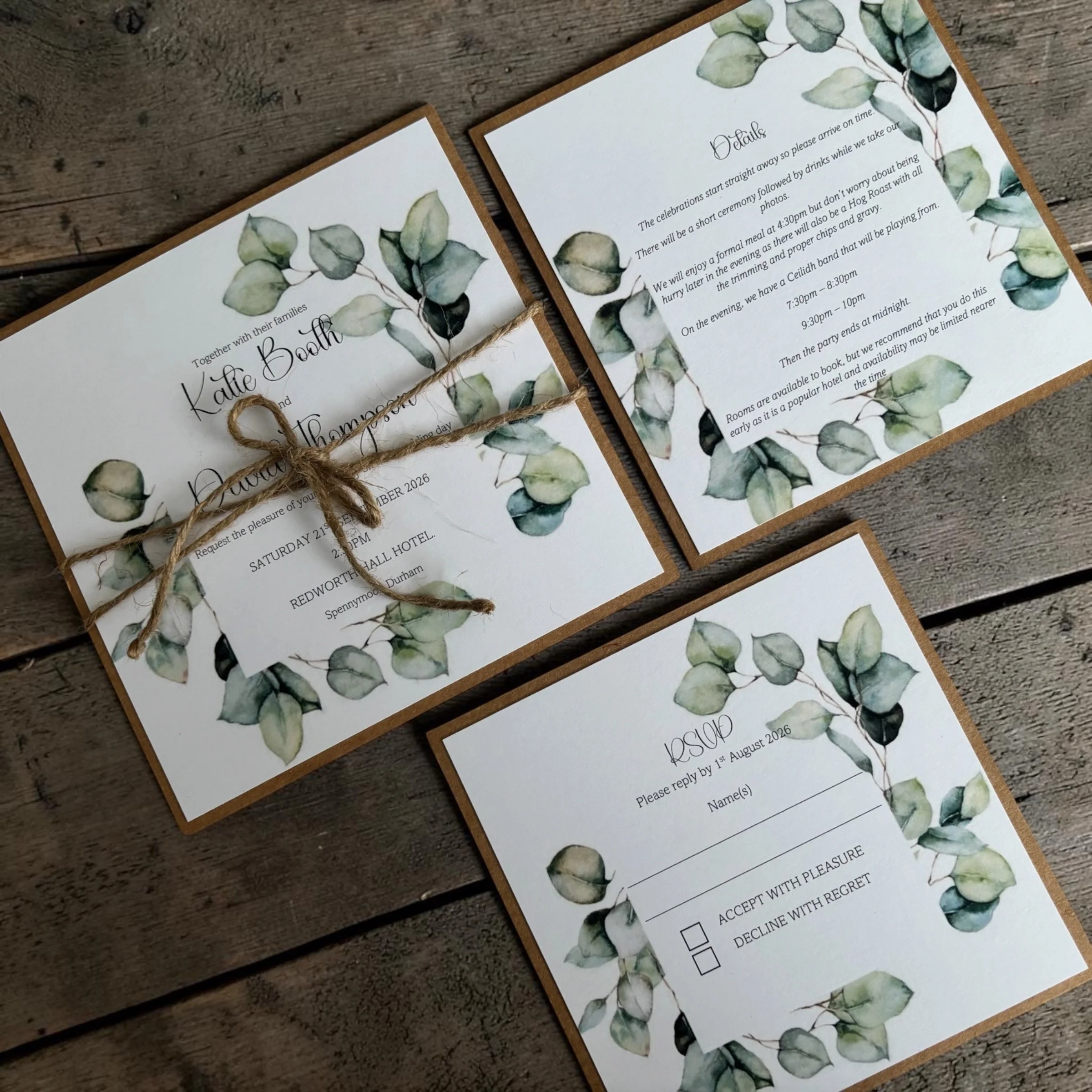 Wedding invitation cards with eucalyptus leaf border on a wooden surface, tied with a string.