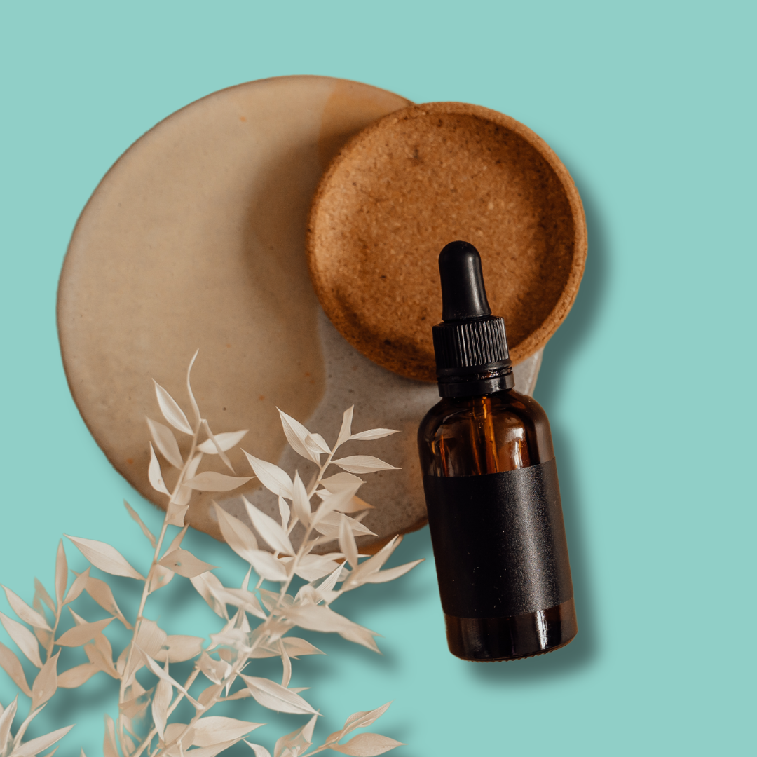 Amber essential oil bottle with dried botanicals arranged on a soft aqua background