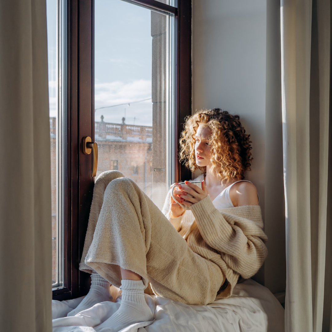 Woman sitting by a window with a warm drink during a quiet self-care moment
