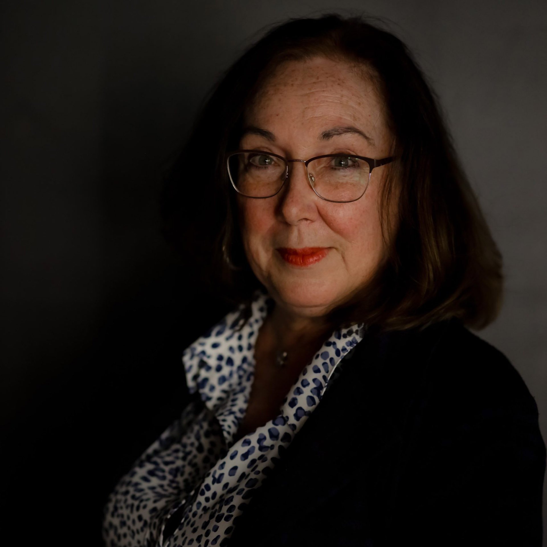 Close-up of a woman with glasses against a dark background.