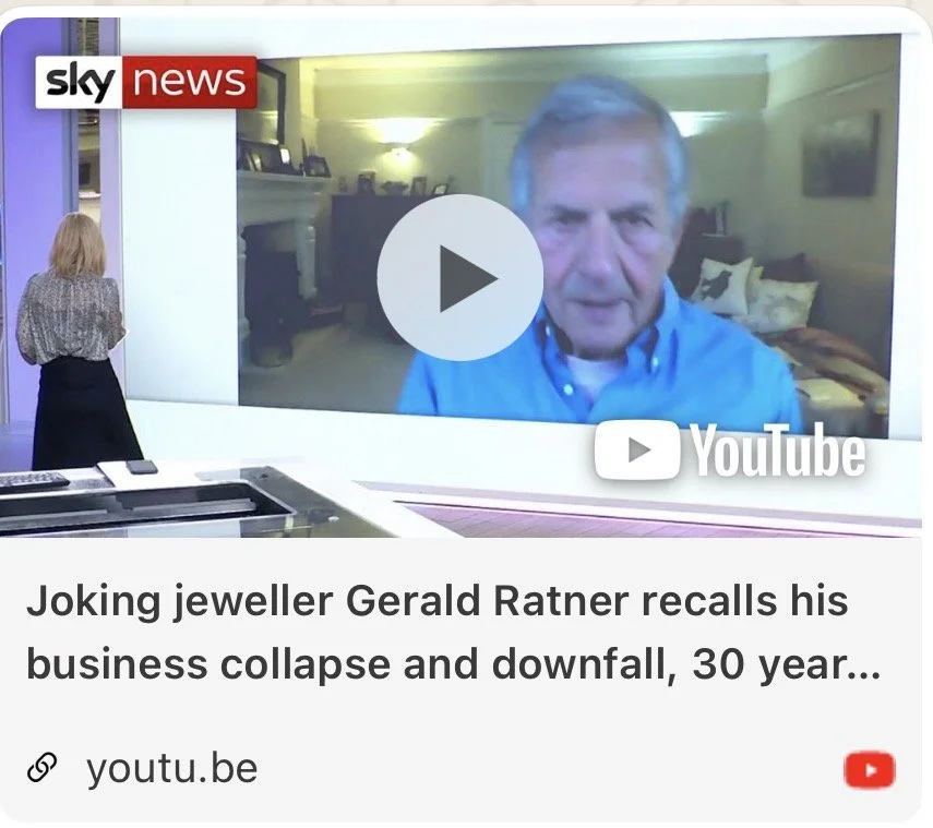 A woman in a patterned blouse and black skirt stands in a studio, looking at a large screen showing a man in a blue shirt during a video interview, with a "Sky News" logo and "YouTube" logo on the screen.
