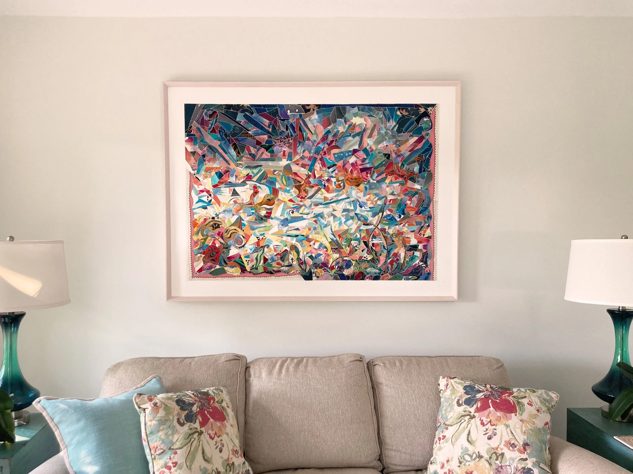 Living room wall decor featuring a colorful abstract mosaic artwork framed above a beige sofa with floral throw pillows and two matching turquoise glass lamps on side tables.