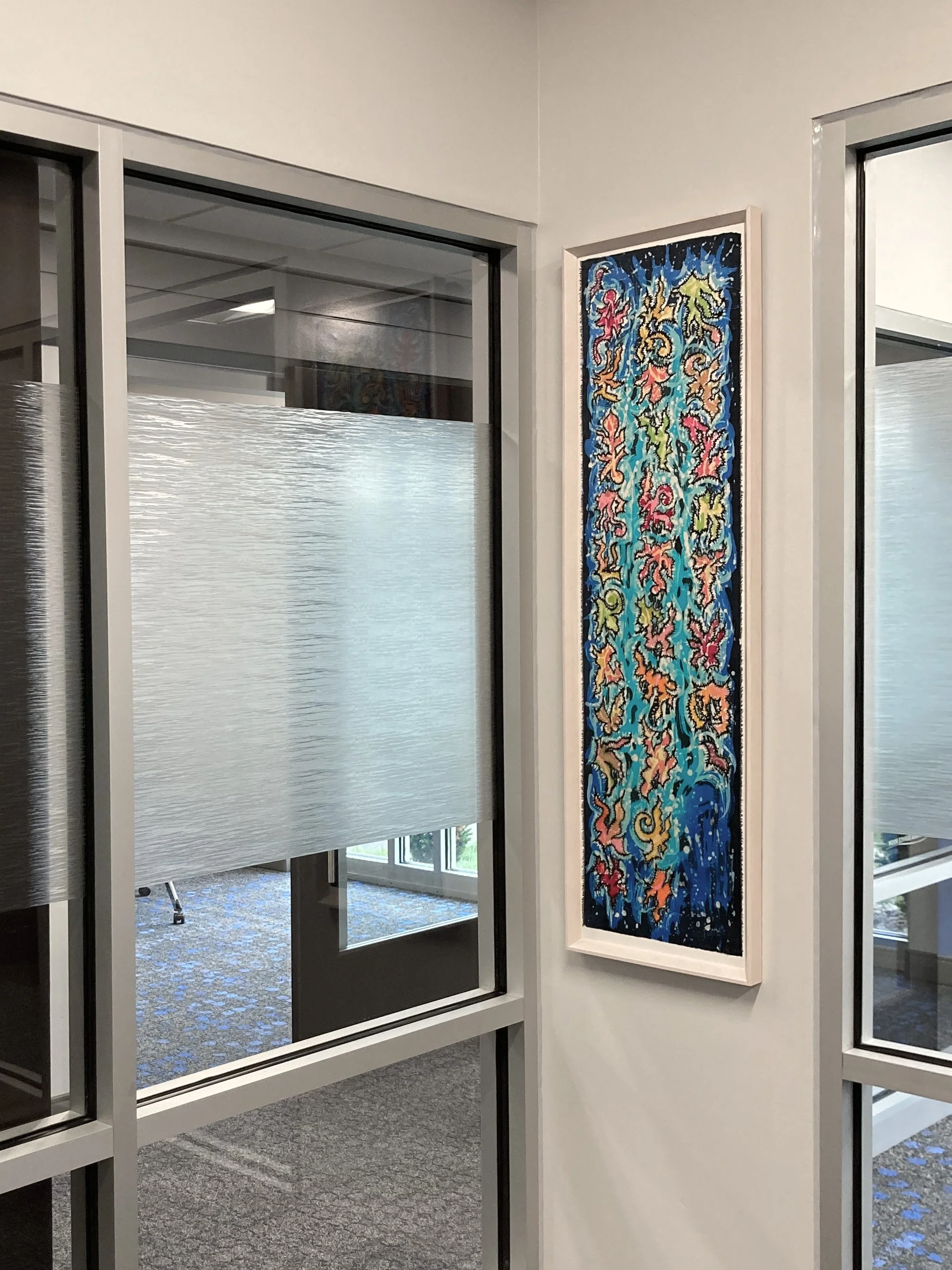 Interior view of an office area with glass partition walls, a colorful abstract artwork hanging on the wall, and carpeted flooring.