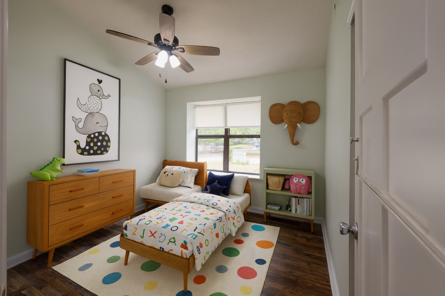 A children's bedroom with light green walls, a wooden bed with a colorful alphabet-patterned blanket, and multicolored polka dot rug. Decor includes a large elephant wall art, a wooden elephant wall hanging, a green dresser with a green dinosaur toy,