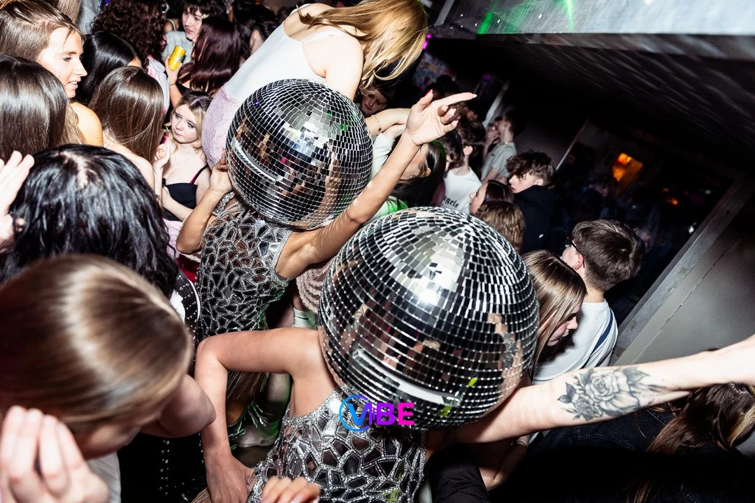 People dancing at a nightclub with disco balls and colorful lights.