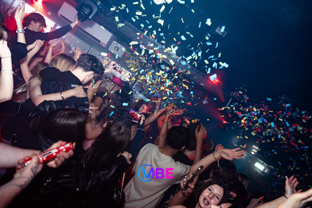 People dancing and enjoying a celebration at a nightclub with colorful confetti falling from the ceiling.