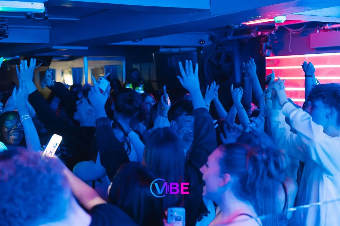 Crowd of people dancing and enjoying music at a nightclub with blue and pink neon lights.