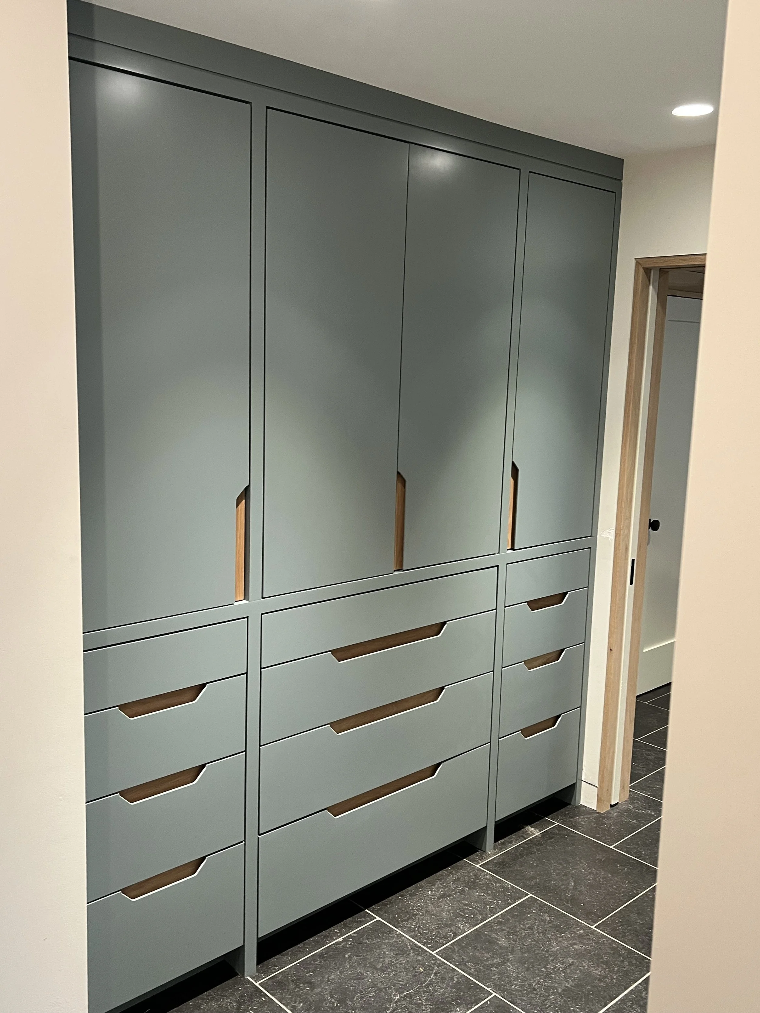 A tall, modern, gray storage cabinet with several doors and drawers, located in a room with black tiled flooring and a plain white wall.