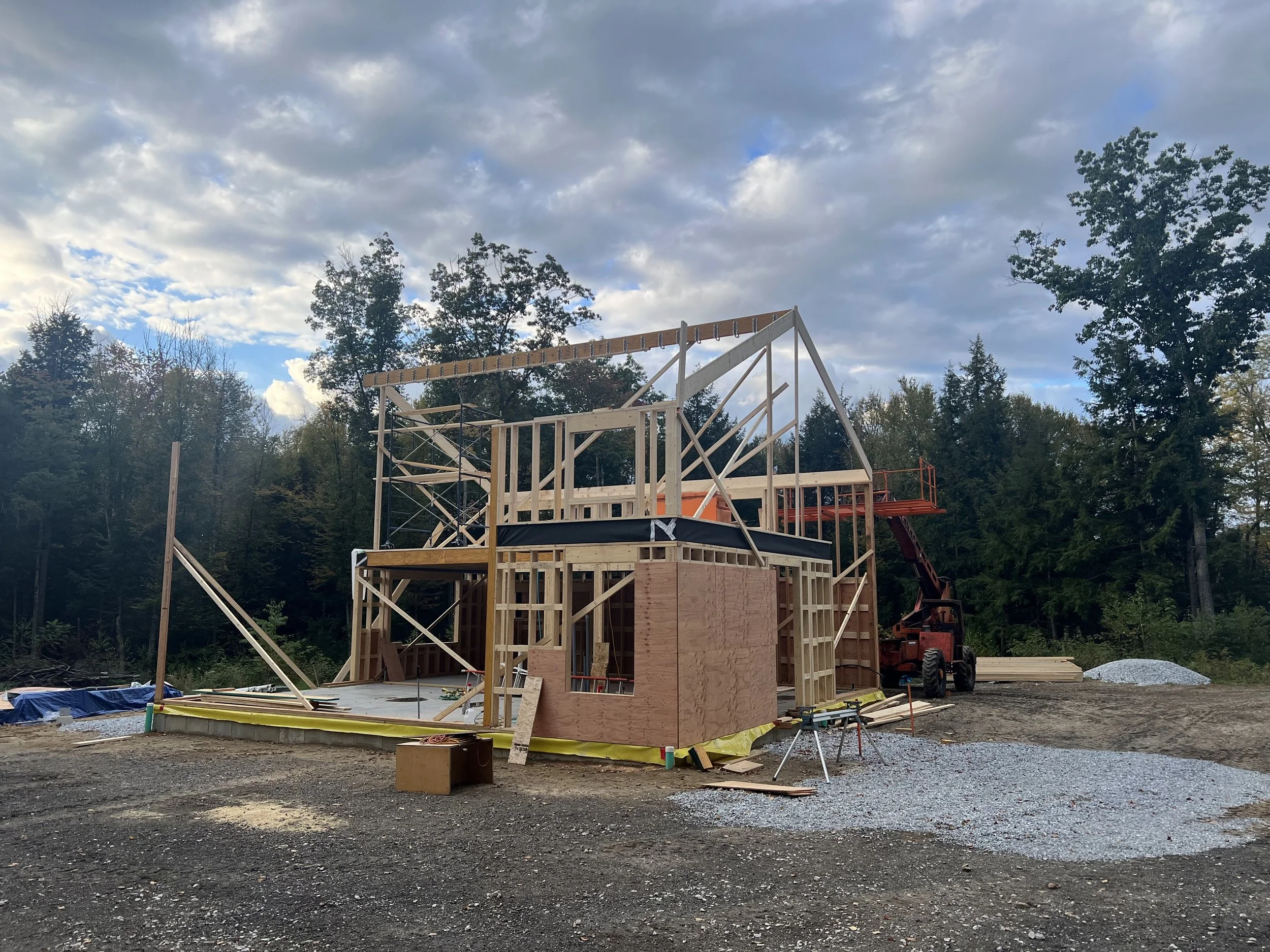 Wooden framework of a house under construction with trees and cloudy sky in the background.