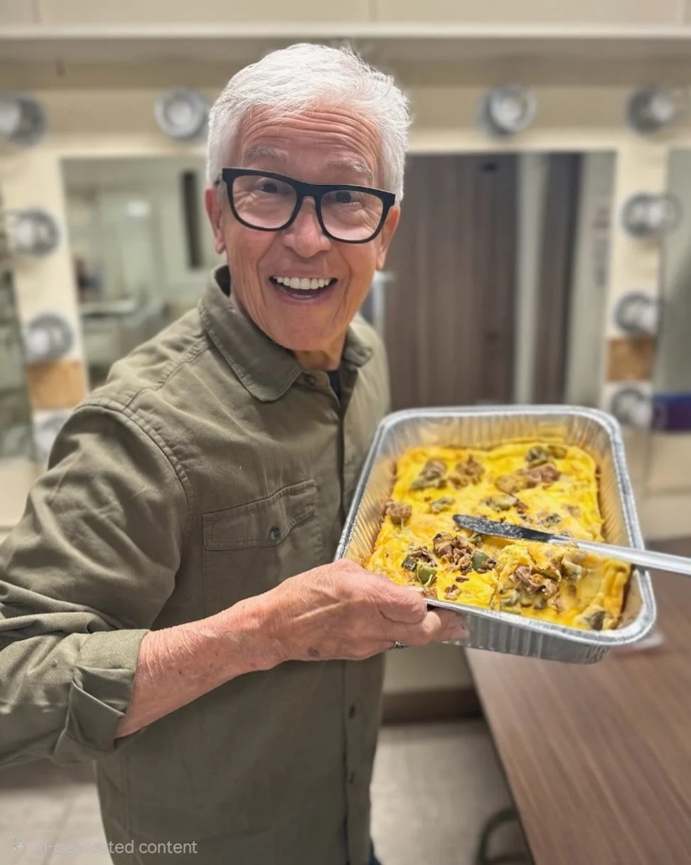 An elderly man with white hair and glasses smiling while holding a tray of baked casserole.