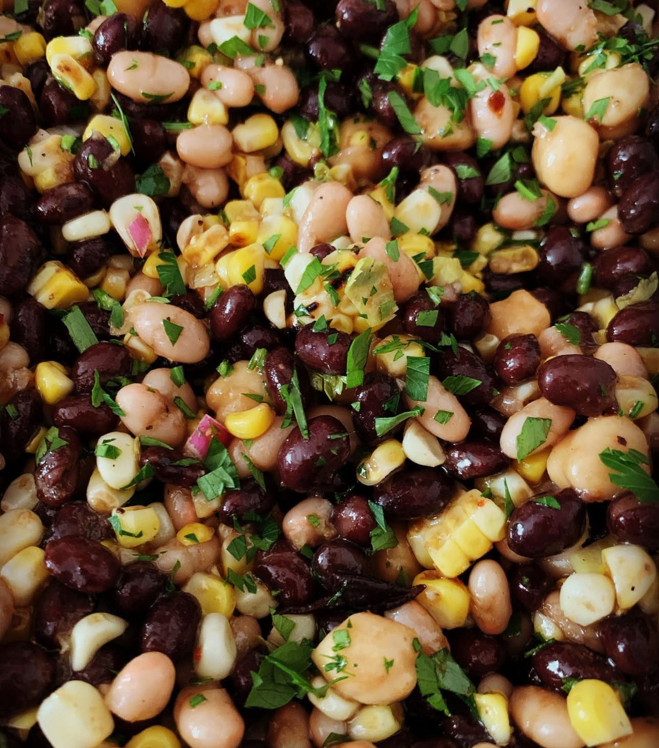 Close-up of a mixed bean salad garnished with chopped herbs.