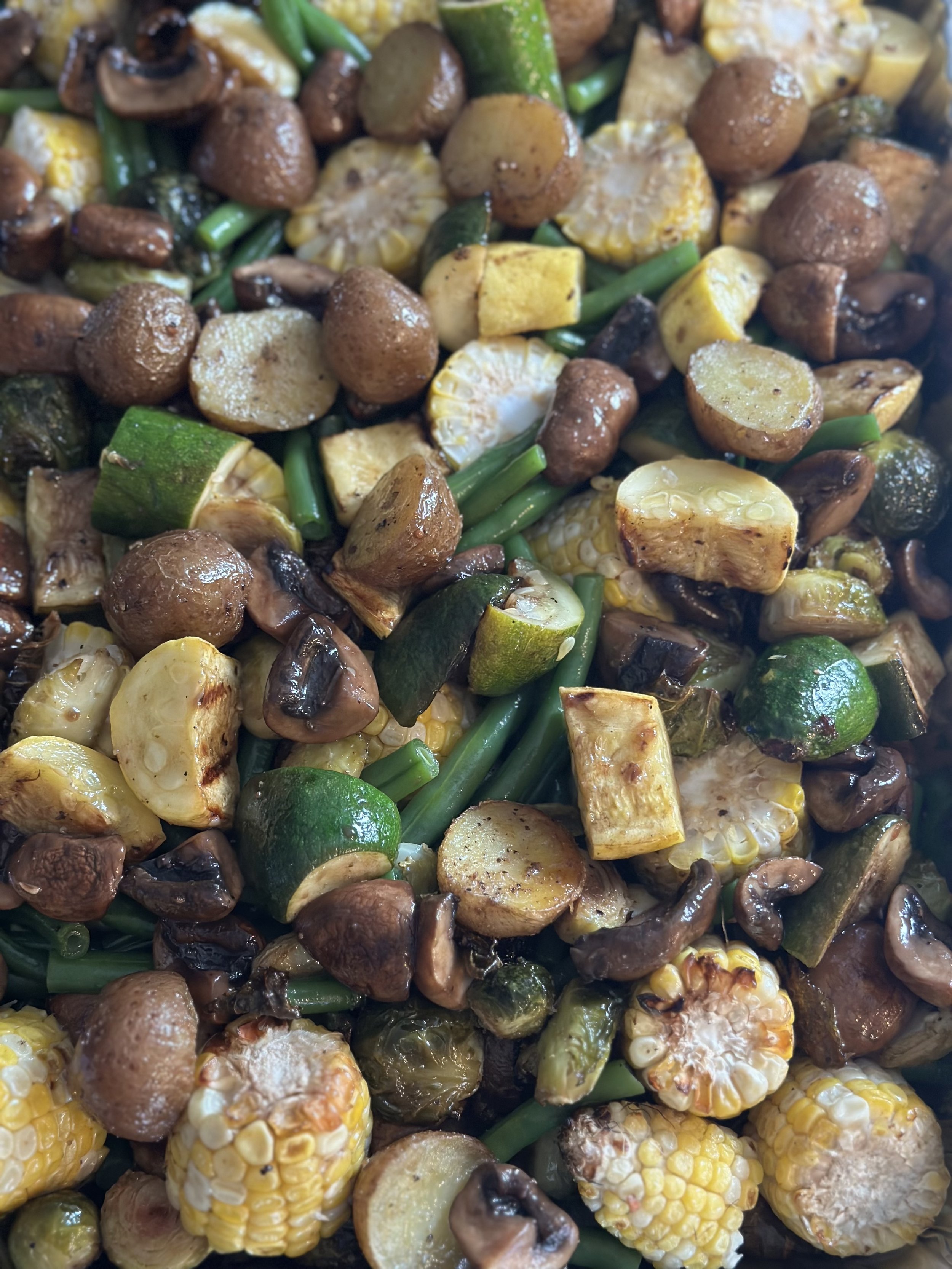 Close-up view of roasted vegetables, including corn on the cob, mushrooms, zucchini, and potatoes.