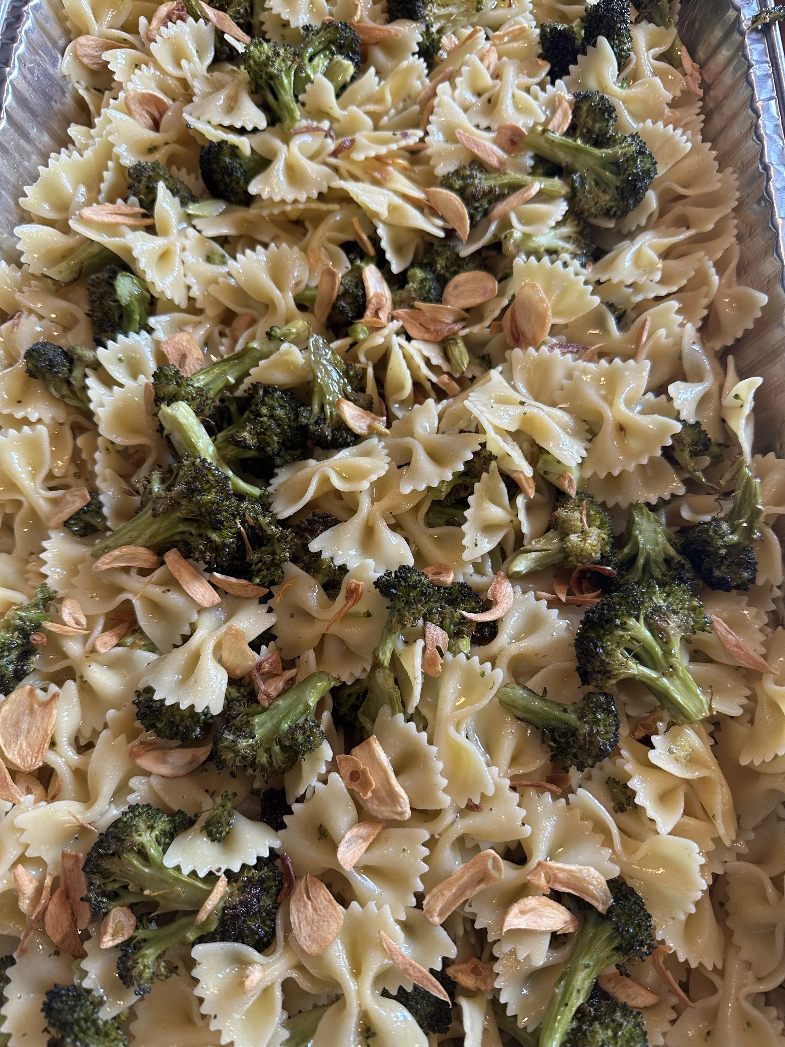 Pasta salad with bowtie pasta, roasted broccoli, sliced almonds, and garlic slices.