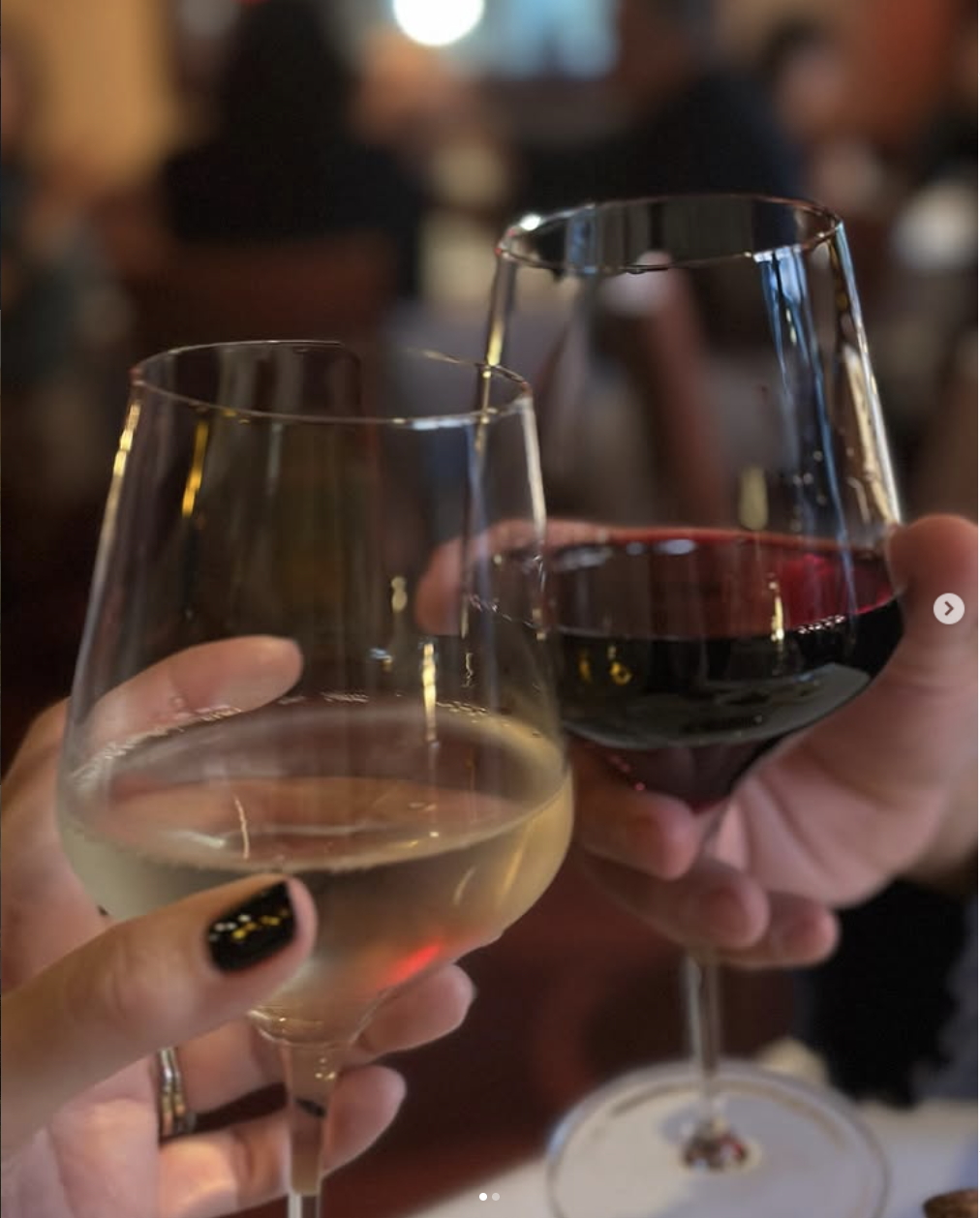 Two people clinking glasses of white wine and red wine at a social gathering.