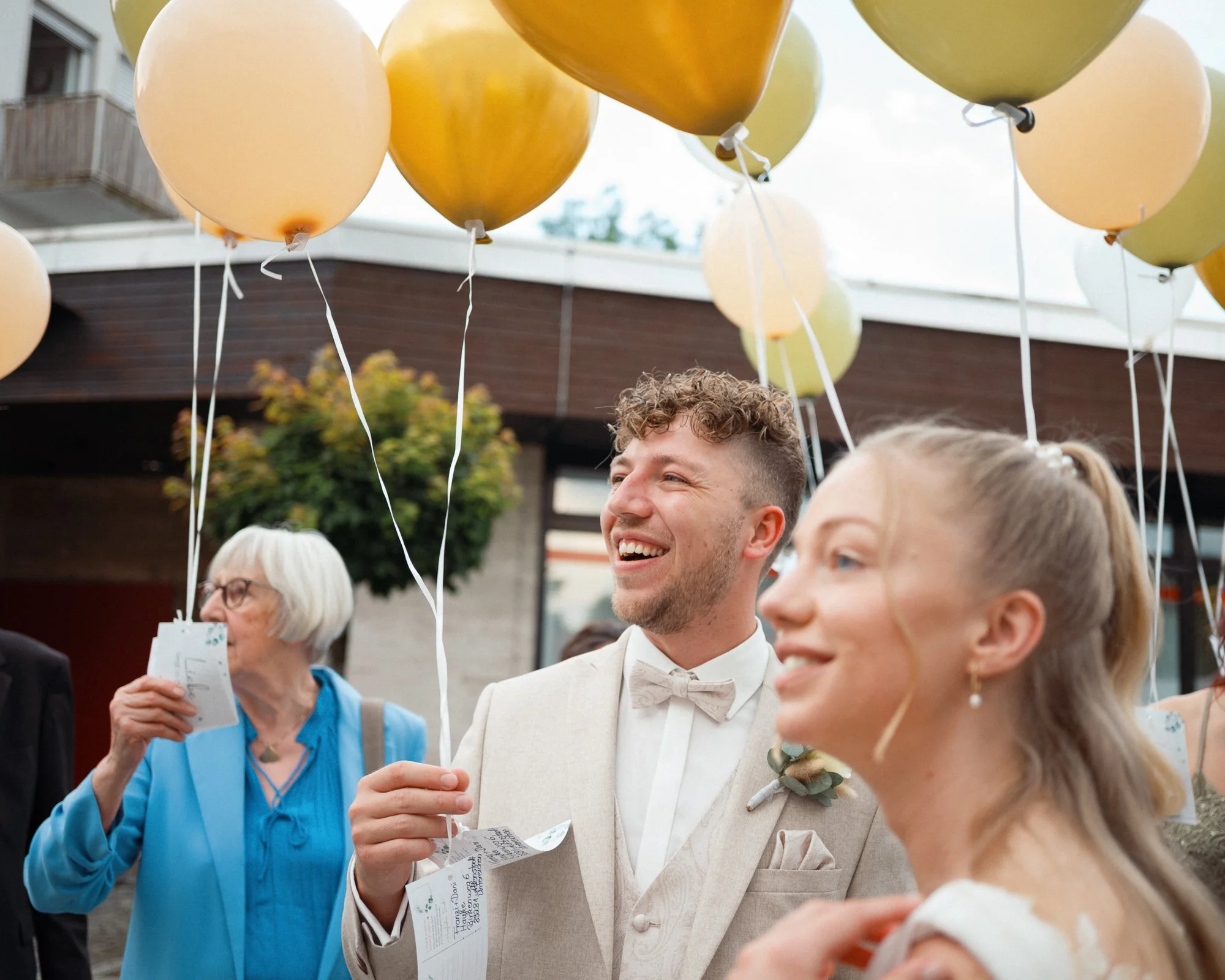 Menschen bei Hochzeitsfeier mit bunten Luftballons im Freien, lachend und fröhlich.