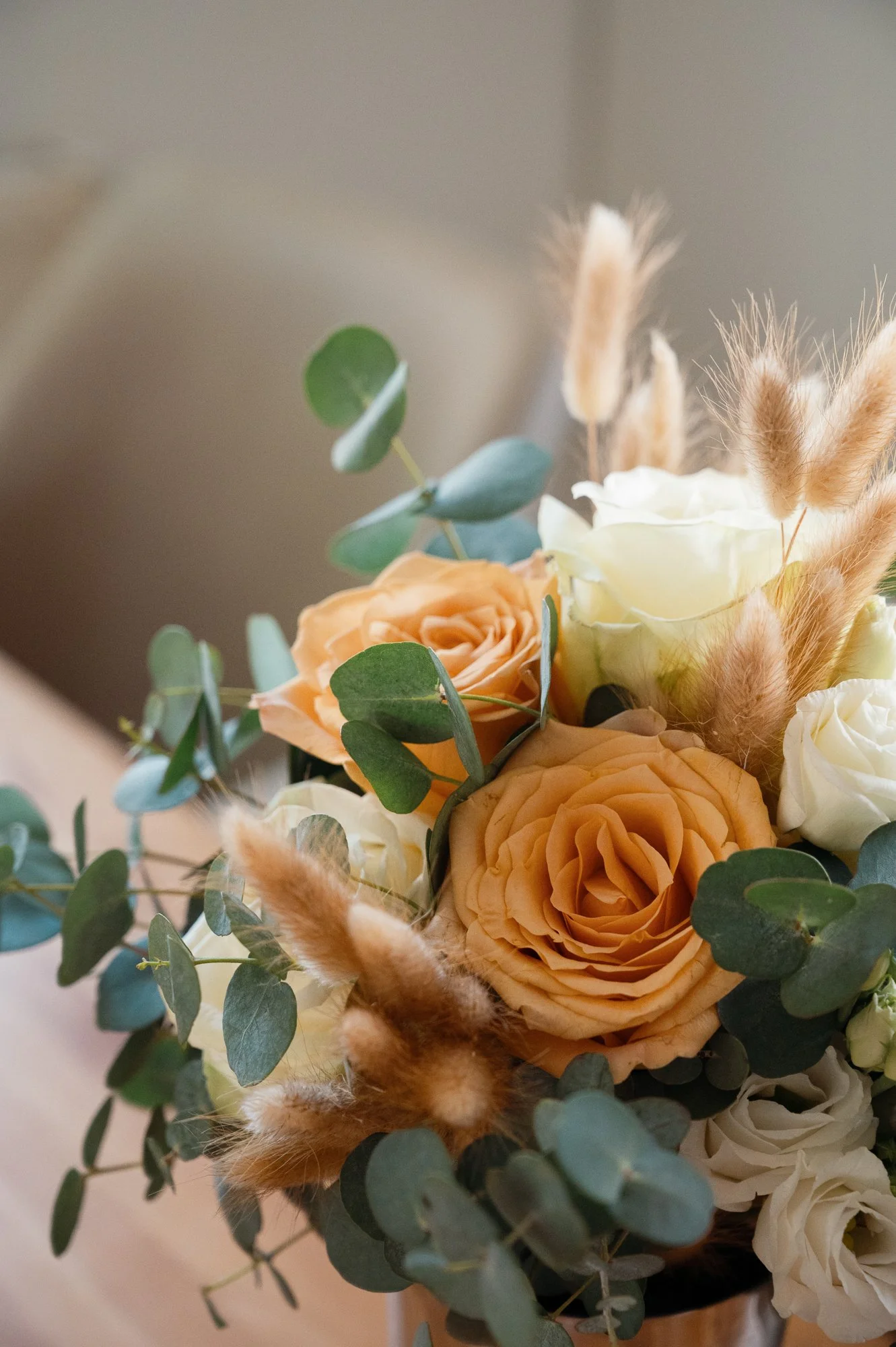 Blick auf einen Blumenstrauß mit cremefarbenen Rosen, peachfarbenen Rosen, grünen Blättern und getrockneten, braunen Gräsern.