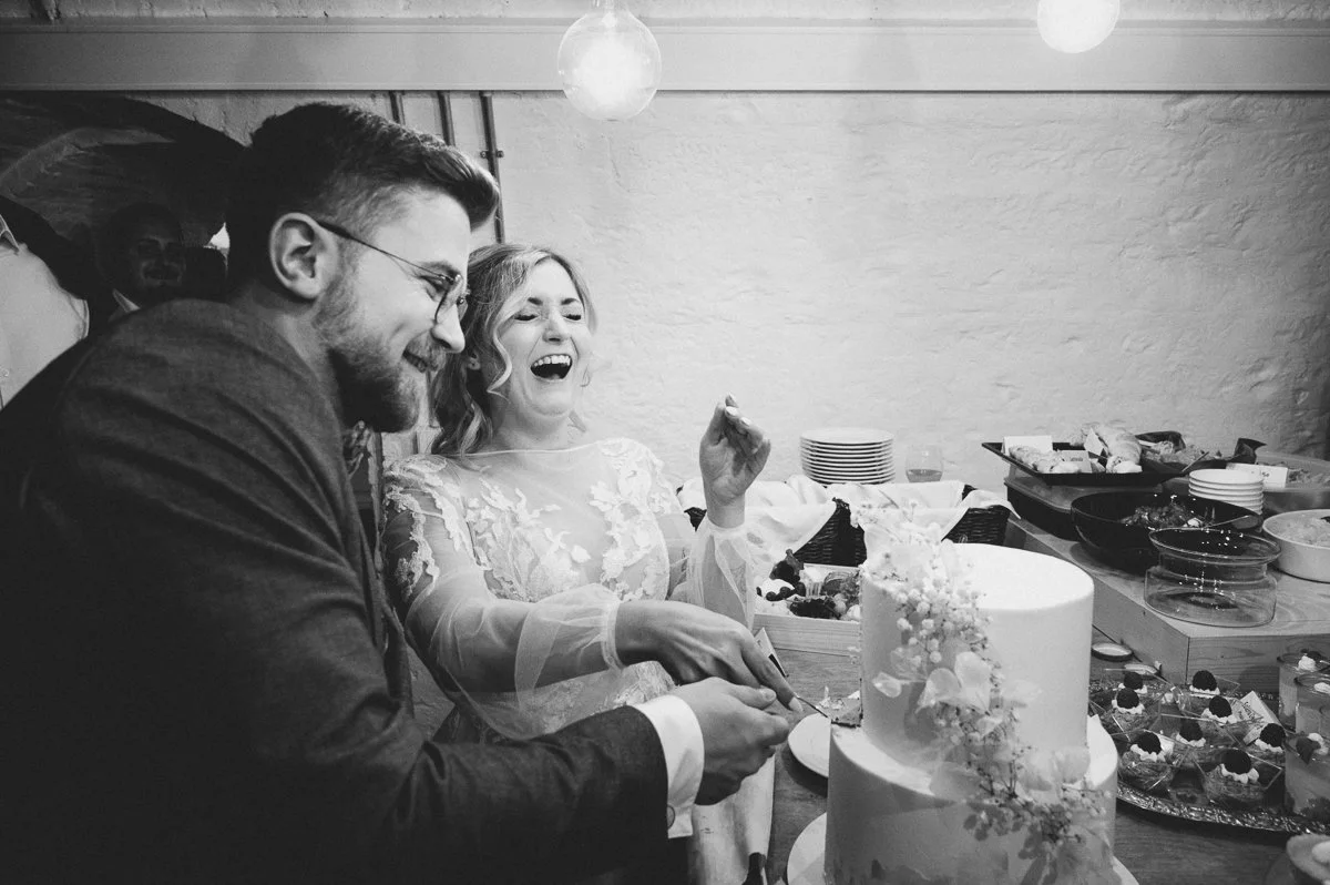 Ein Mann und eine Frau bei einem Hochzeitstag, die zusammen auf eine Torte schneiden, umgeben von Essen und Dekorationen.