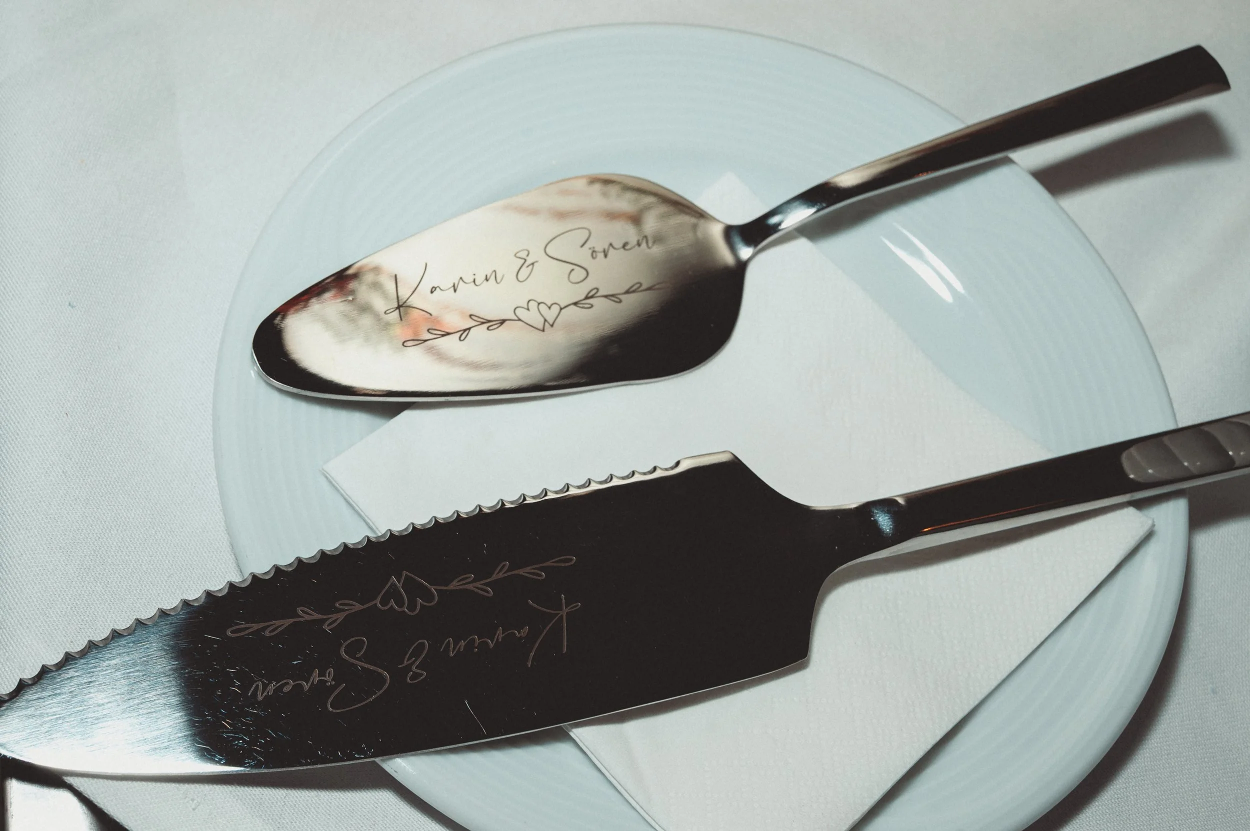 Ein Messer liegt auf einem weißen Teller. Auf dem Messer ist eine Gravur mit dem Namen "Karin & Sören" und einem Herz. Das Messer ist in einem schwarzen Etui verpackt.
