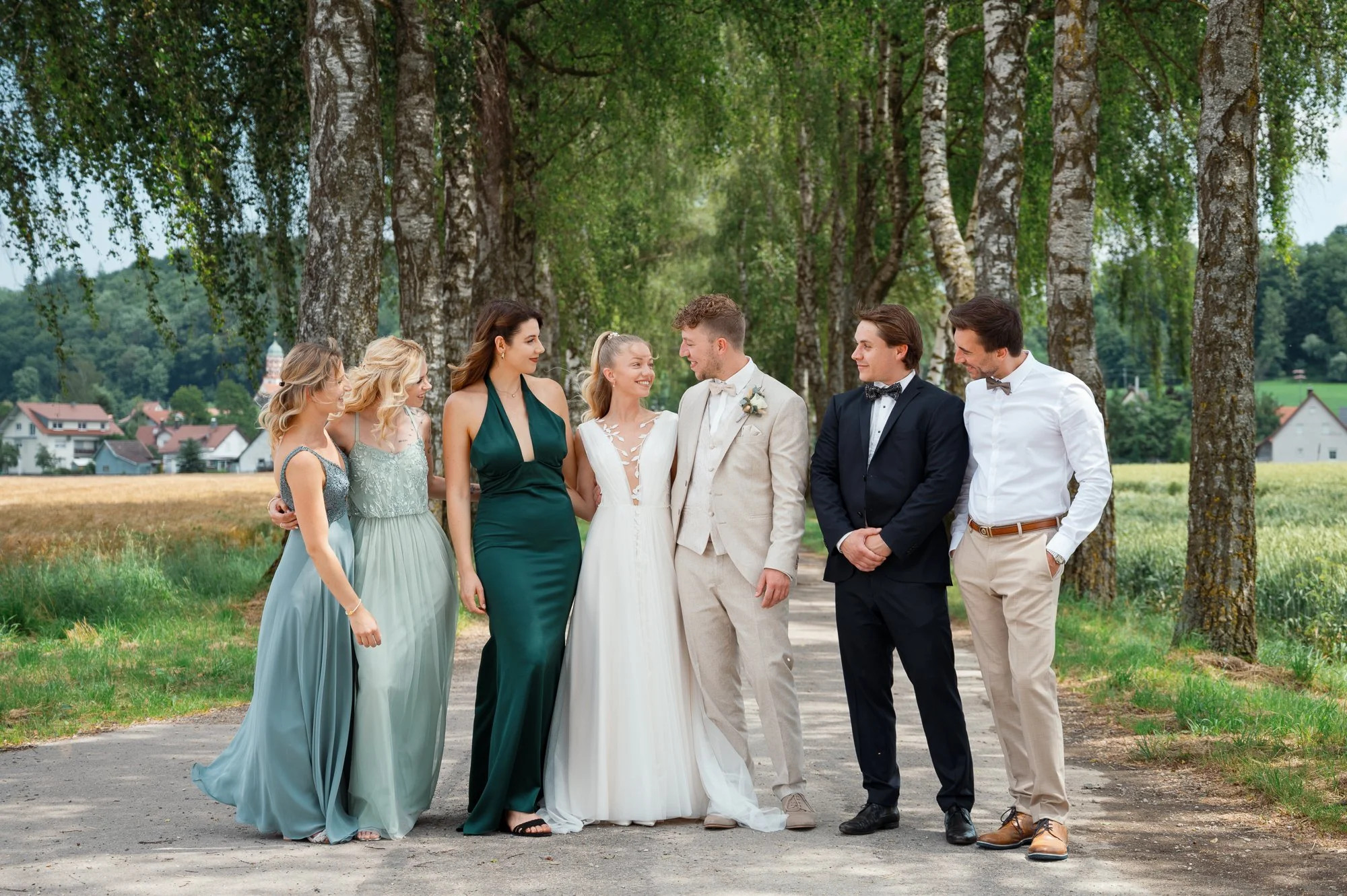Hochzeitspaar mit vier Frauen und zwei Männern im Freien, umgeben von Bäumen.