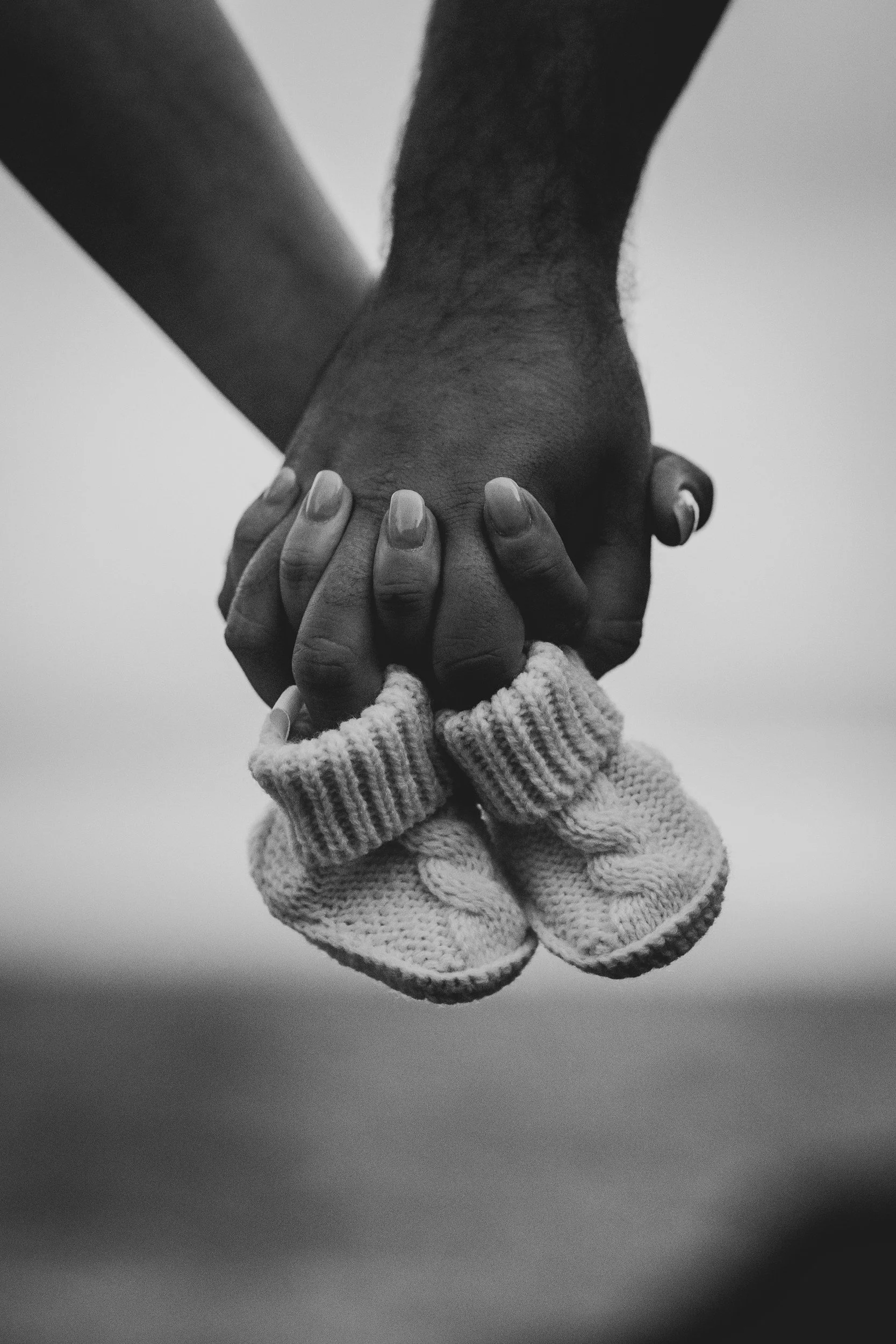 Close-up of two hands holding each other, one wearing a knitted sweater and the other with a darker skin tone, in black and white.