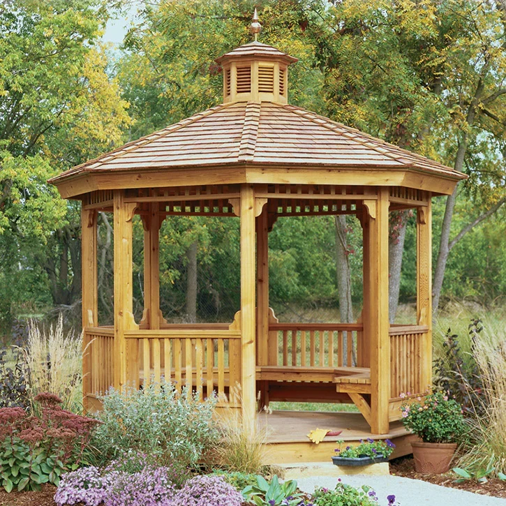 Wooden gazebo with a shingled roof, surrounded by colorful flowers and plants in a garden.