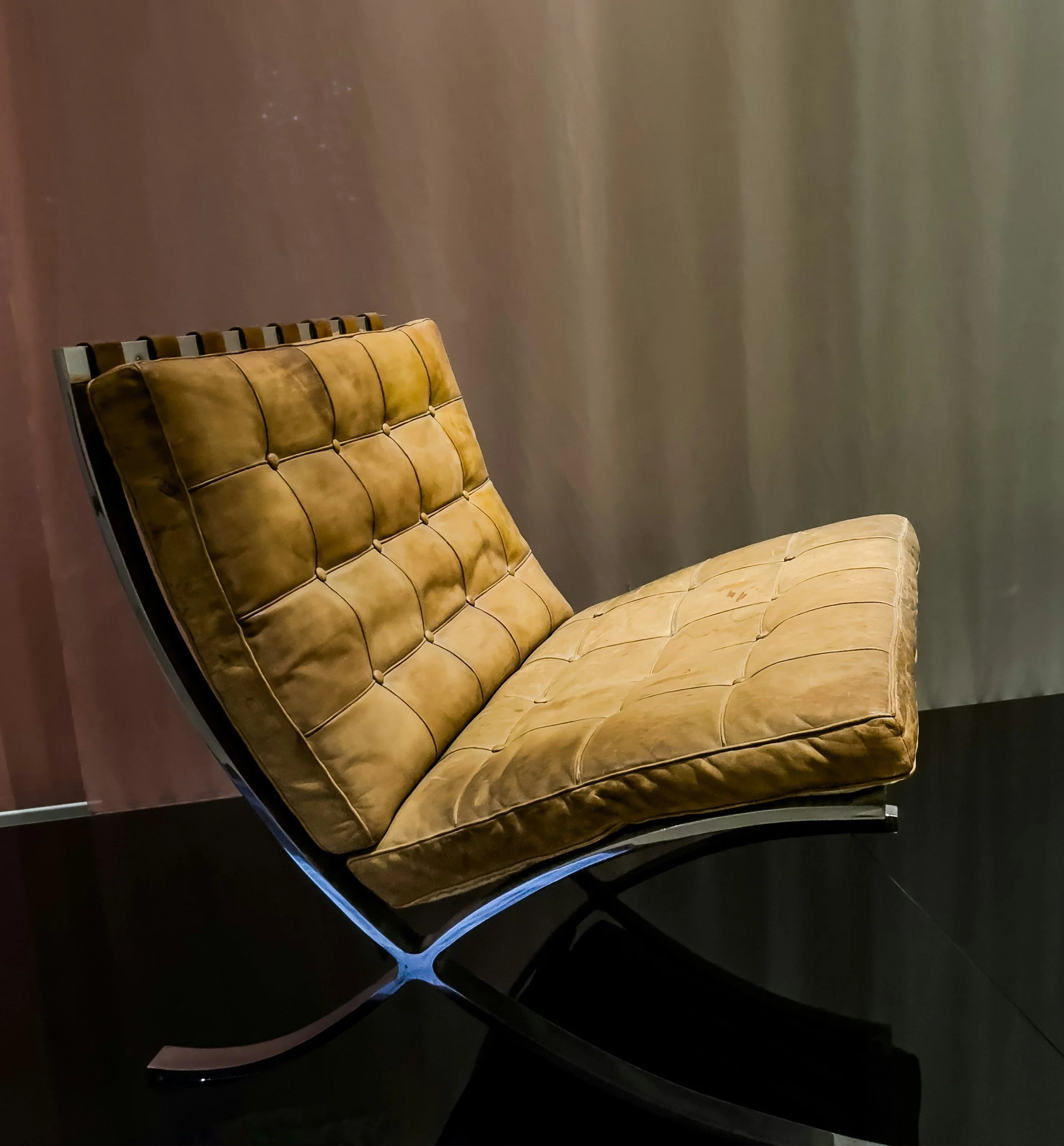 A yellow leather lounge chair with a black metal frame and wooden slats on the backrest, positioned against a plain wall and on a dark floor.