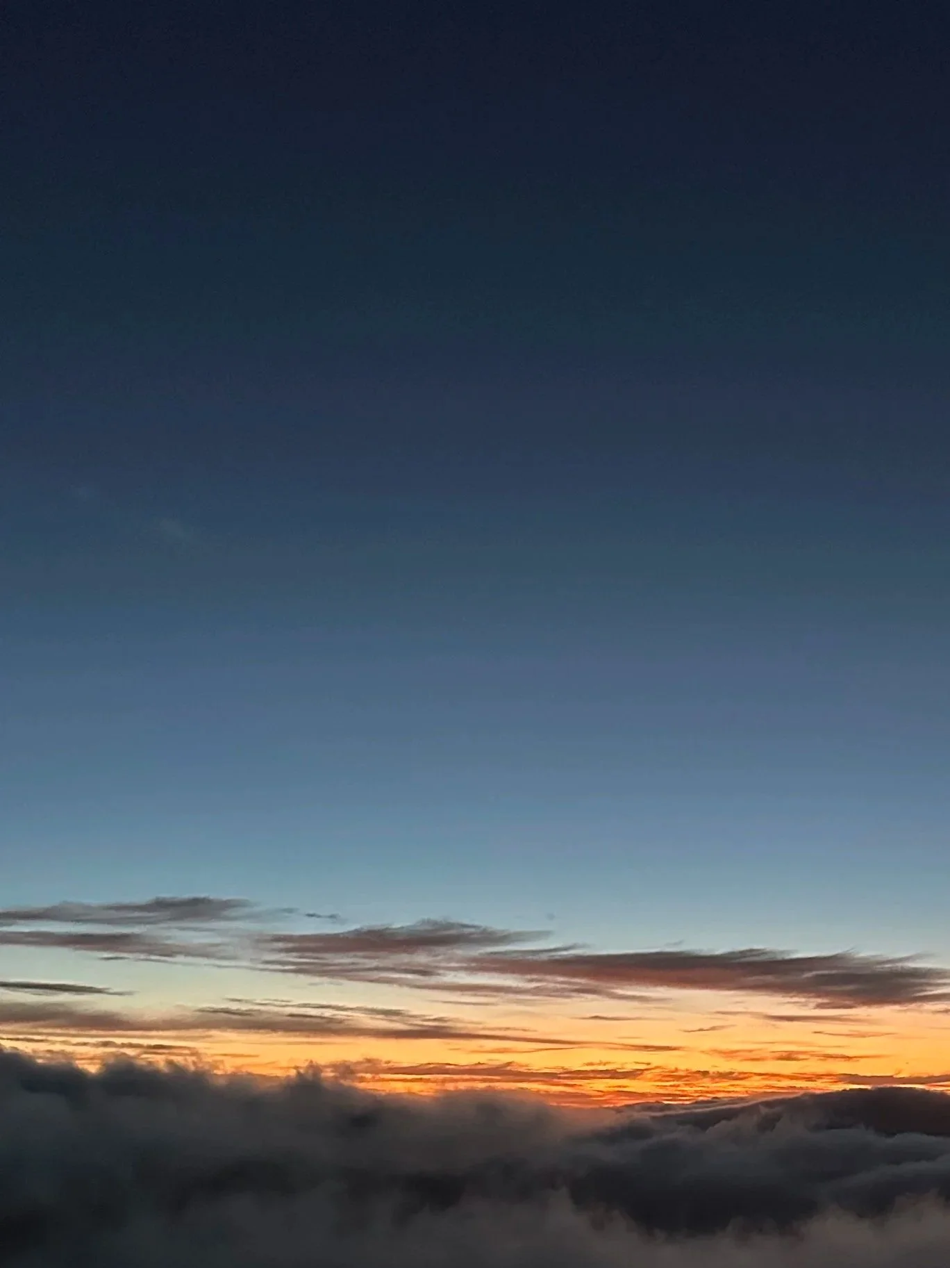 Sky at sunset with layers of clouds and a gradient of colors from dark blue to orange near the horizon.