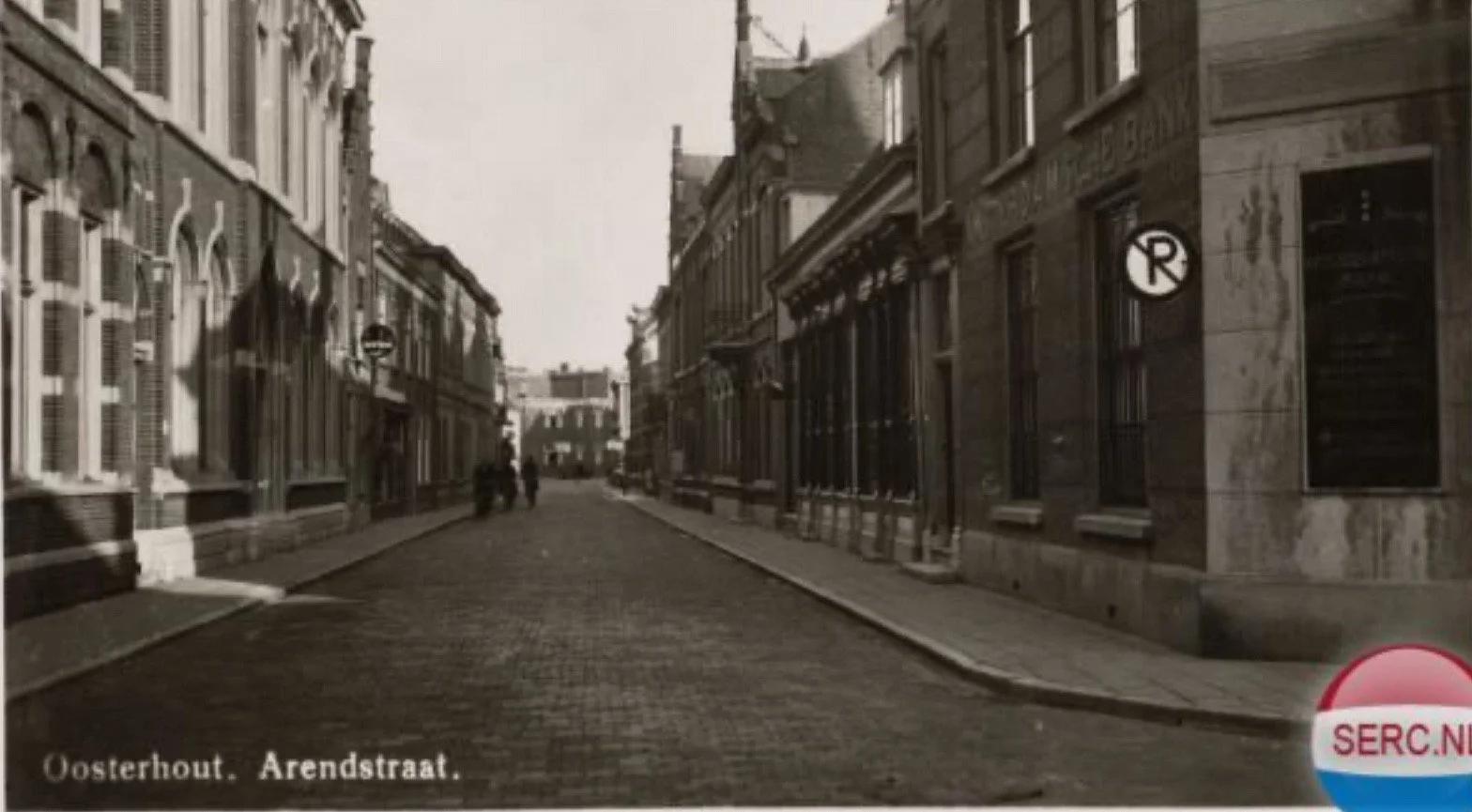 Een historische zwart-witfoto van een straat in Oosterhout, Arendstraat, met oude gebouwen aan weerszijden en een paar mensen wandelend in de verte.