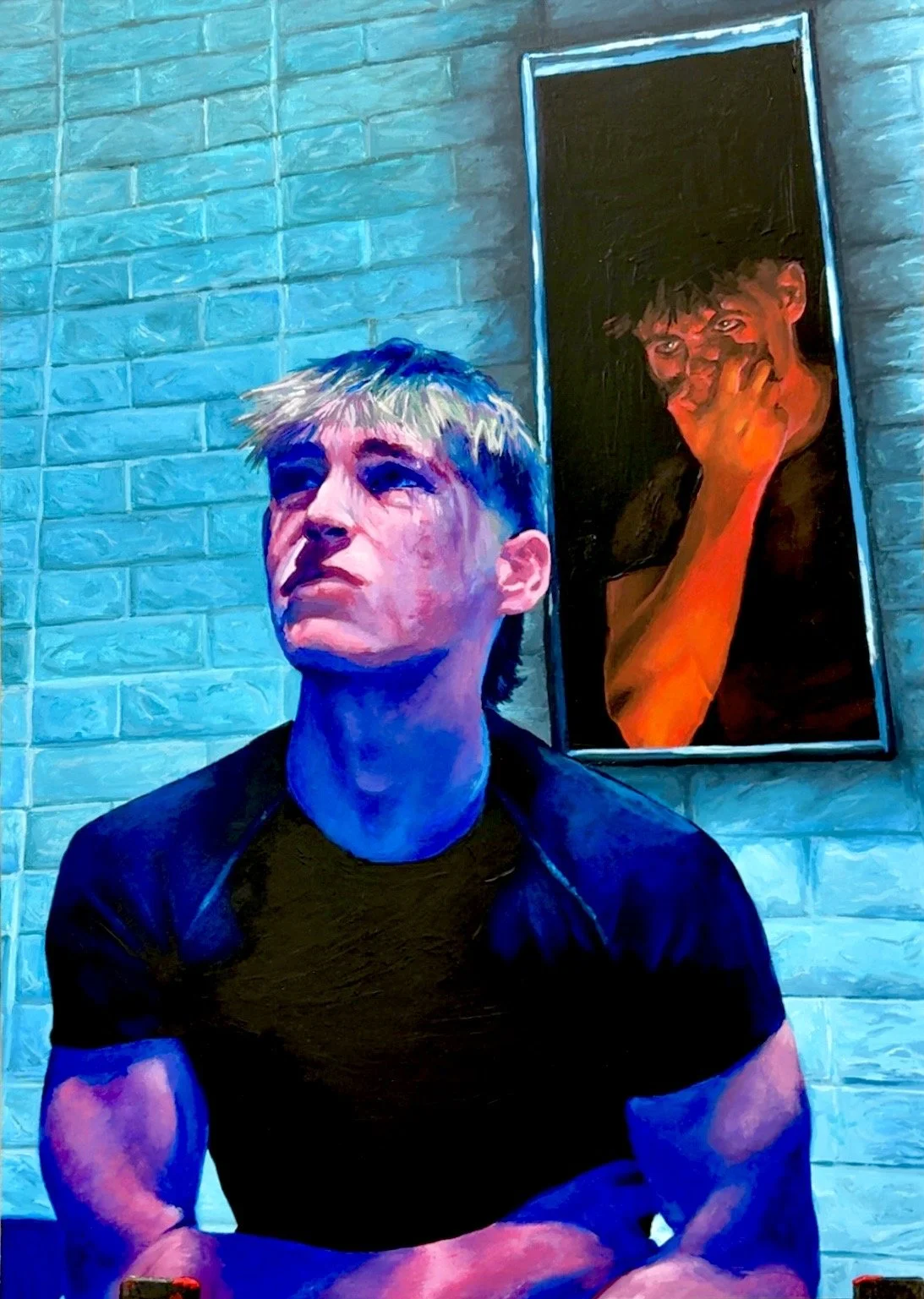 A young man with blond hair and a black shirt sitting in front of a white brick wall, with a colorful portrait painting of a person with short dark hair and an orange hand covering their mouth hanging behind him.