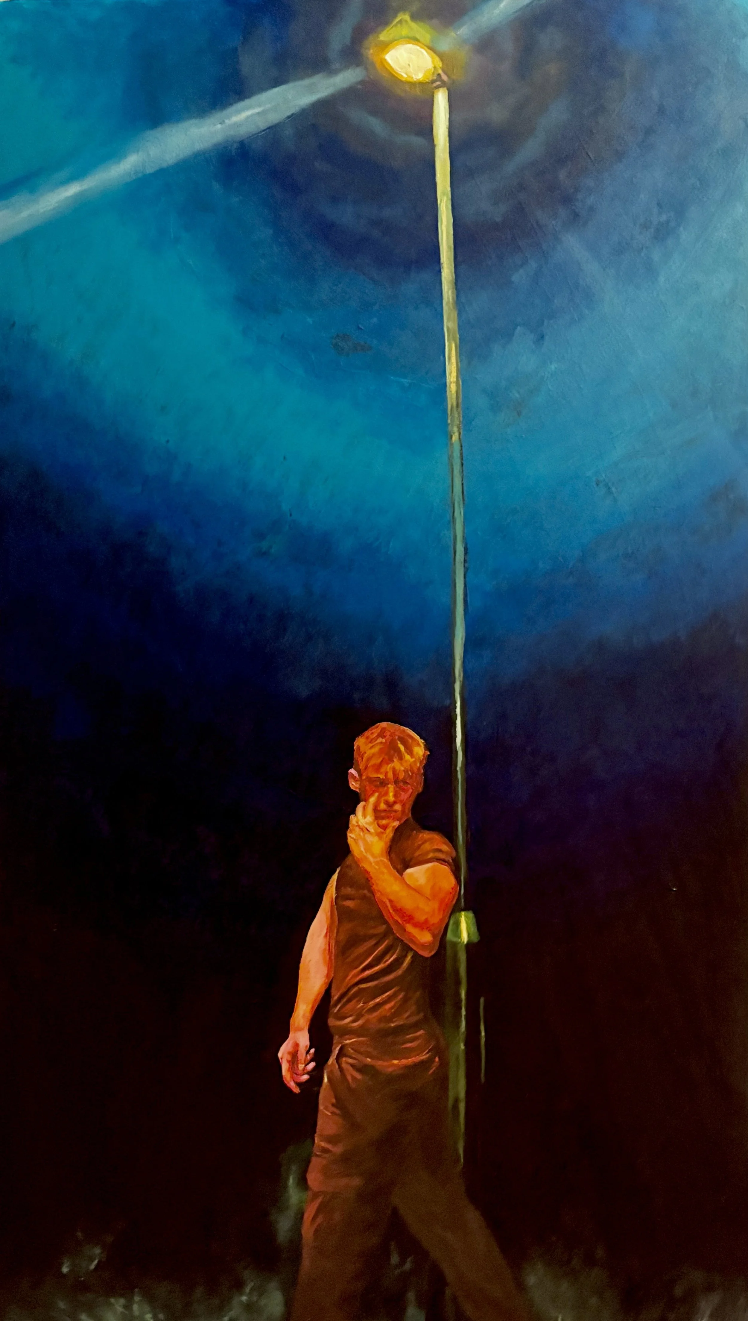 A man with short hair, wearing a dark t-shirt and pants, poses with his left hand touching his chin and his right hand hanging down. Behind him, a tall street lamp extends upward, and the background features a dark, cloudy night sky with a bright light or moon in the distance.