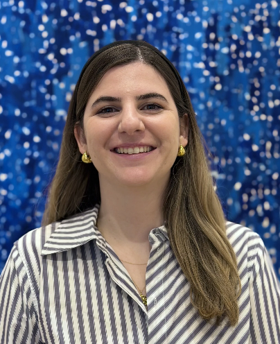 A woman with long brown hair, wearing gold earrings and a striped shirt, smiling in front of a blue background with white sparkles.
