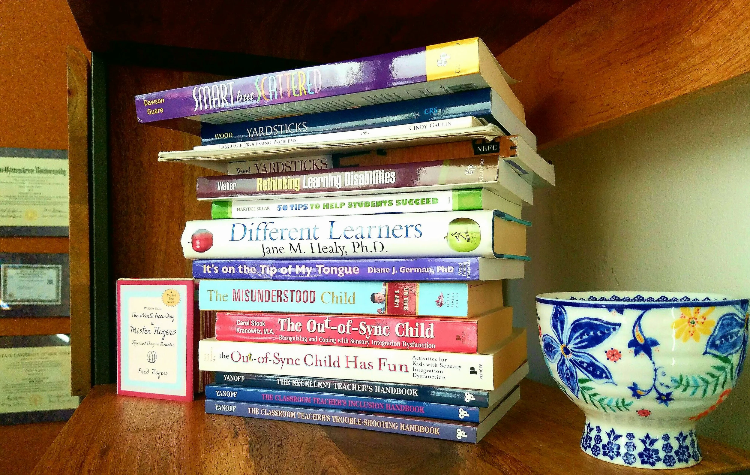 Stack of educational and self-help books on a wooden surface, including titles on learning disabilities, sensory integration, classroom management, and child development, with a decorative ceramic vase nearby.