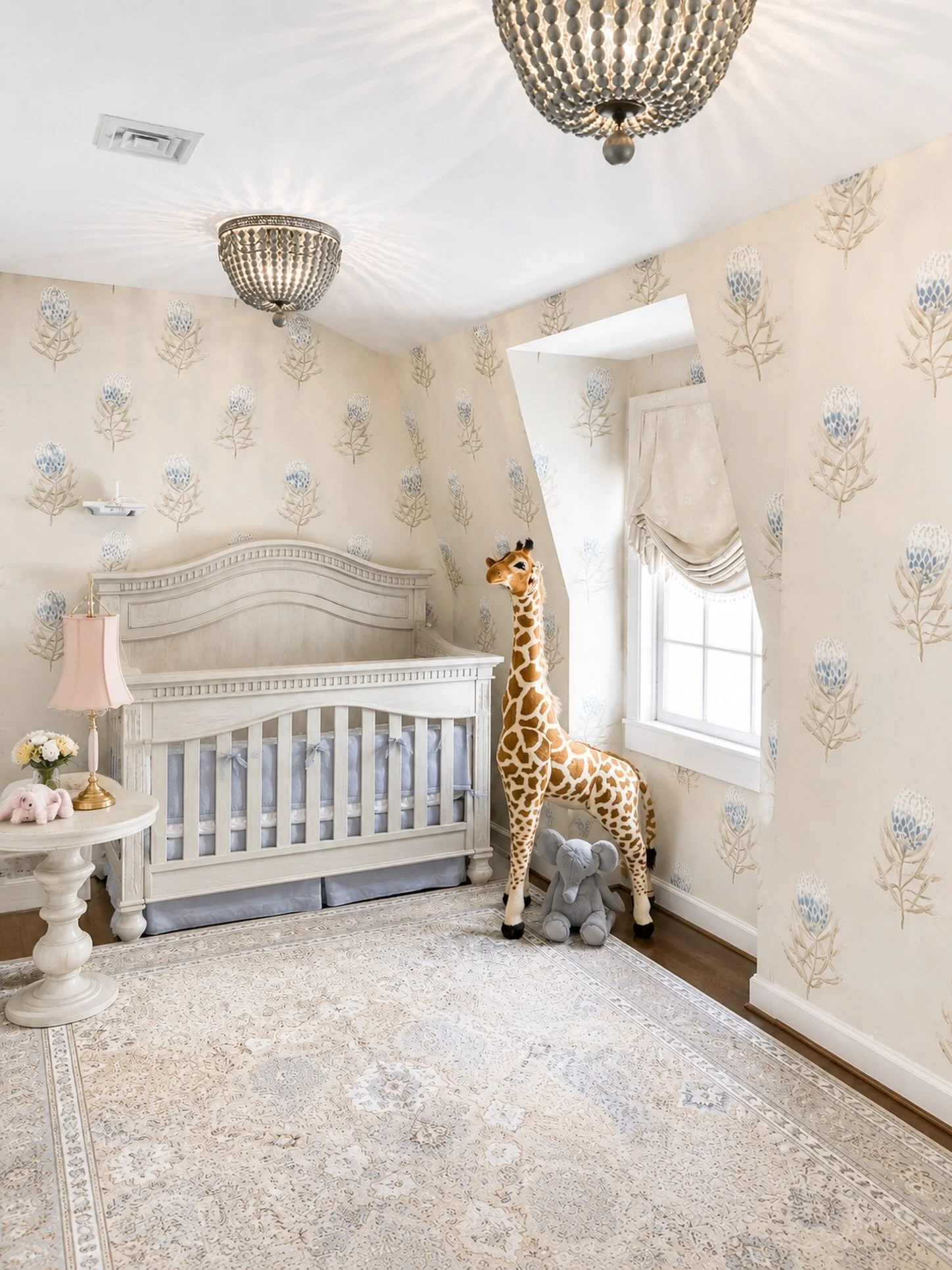 A small, sweet moment where light neutrals create a soft space this nursery.  Texture in lighting, patterns in rug and wallpaper, and a soft Roman window treatment, combine complexity in layers while staying inviting and comforting. #ridgewooddesigns