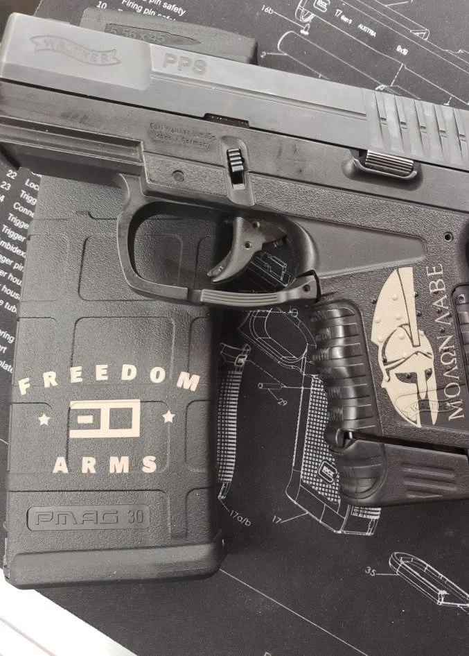 A semi-automatic handgun with a black grip and grey slide, resting on a black Freedom Arms case and a gun cleaning mat with schematic diagram.