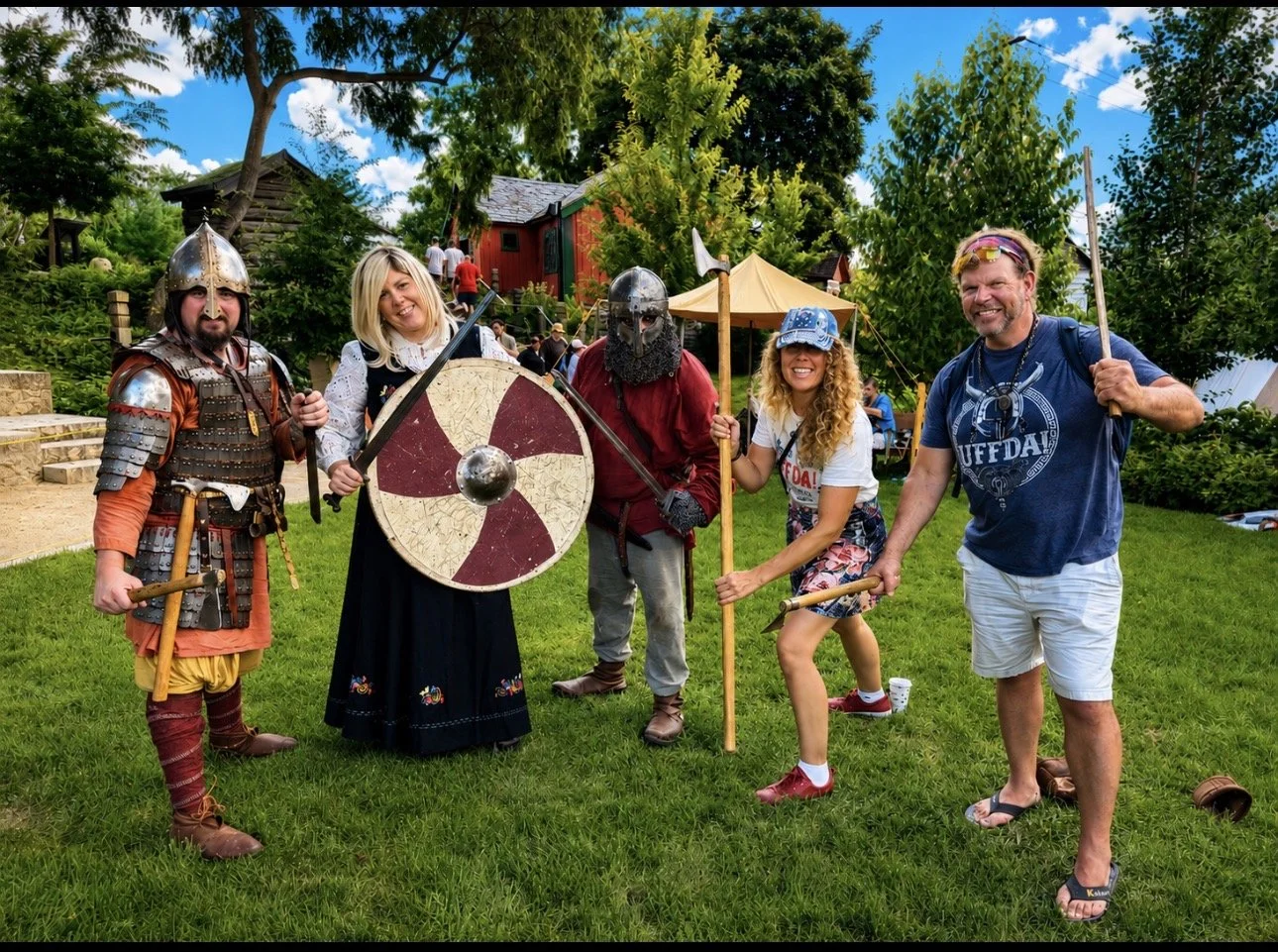 People dressed as medieval warriors and characters, smiling and posing outdoors with green grass and trees in the background, during a medieval-themed event.