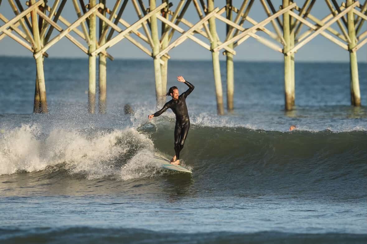 A person surfing on a wave near a wooden pier over the ocean.