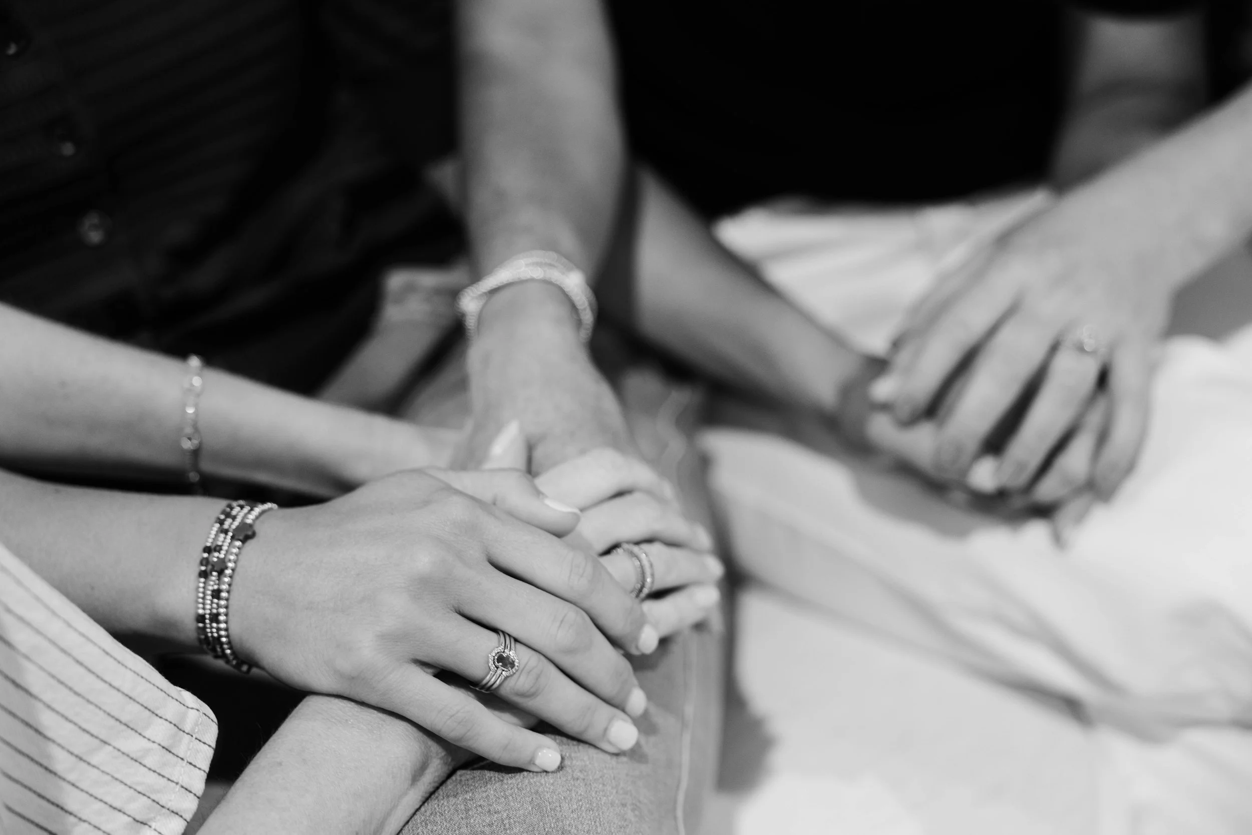 Close-up of several hands placed on top of each other, showing jewelry like rings and bracelets, suggesting unity or friendship.