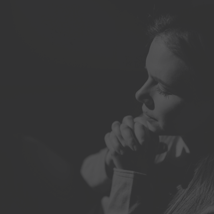 A woman with long hair is seen in profile, with her hands clasped together near her face, appearing to be deep in thought or prayer, in a black and white photo.