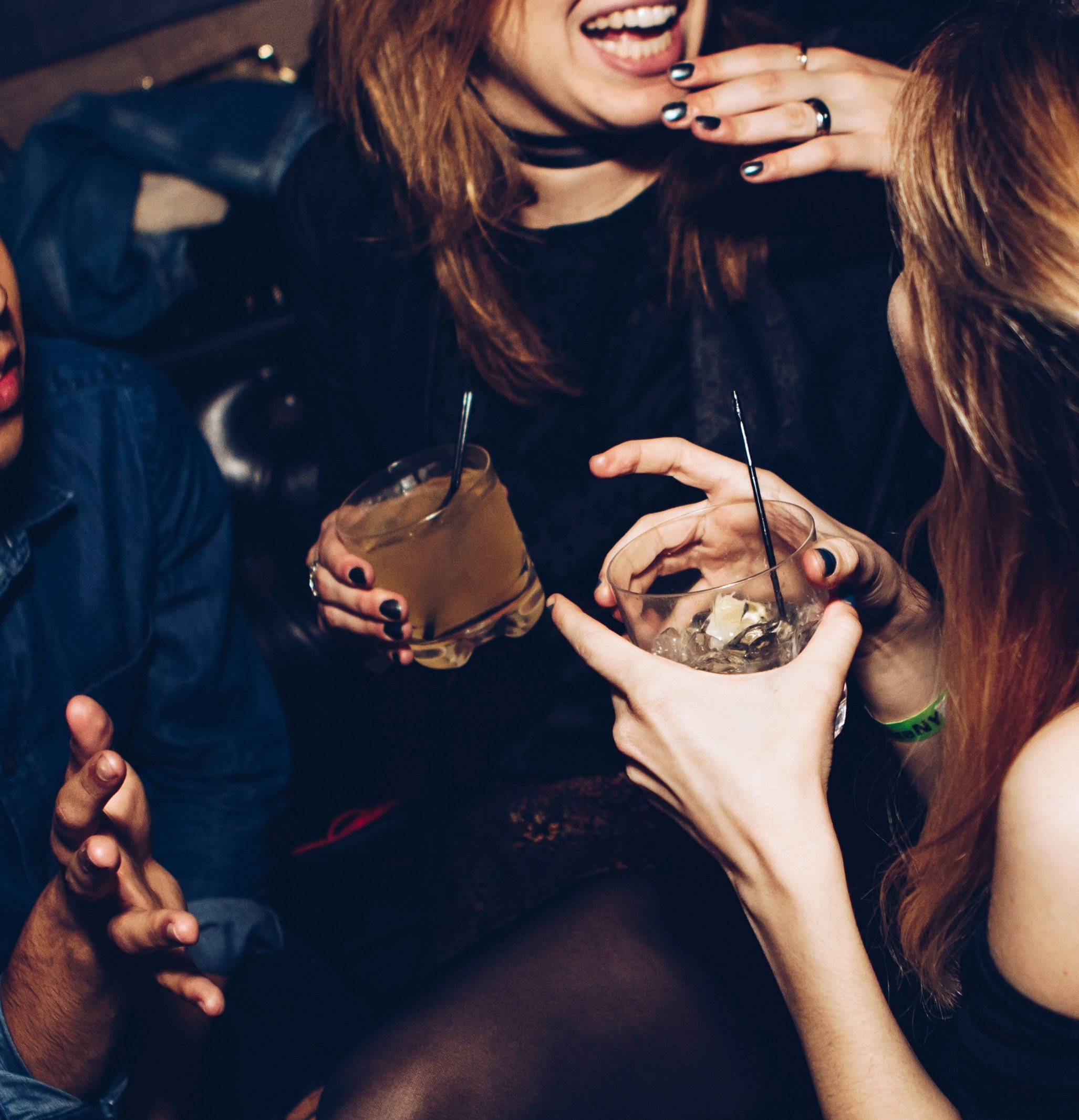 People sharing drinks at a social gathering, with one person wearing a leather jacket and another with long hair, their faces partially visible.