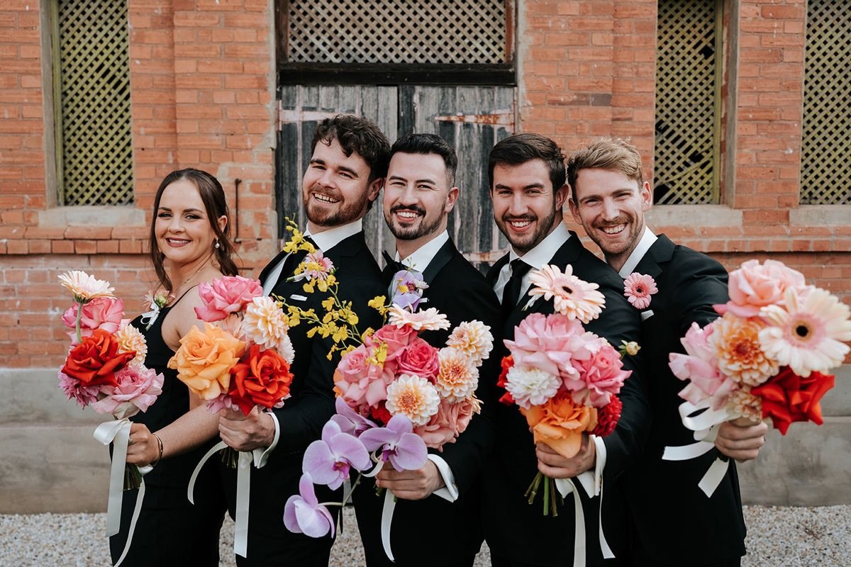 Love this pic of the grooms bridal party with the bridesmaid bouquets, everyone lined up, flowers up, big happy grins.
These ones had roses, dahlias, gerberas all running through every single bouquet &mdash; tied it all together without making anyone