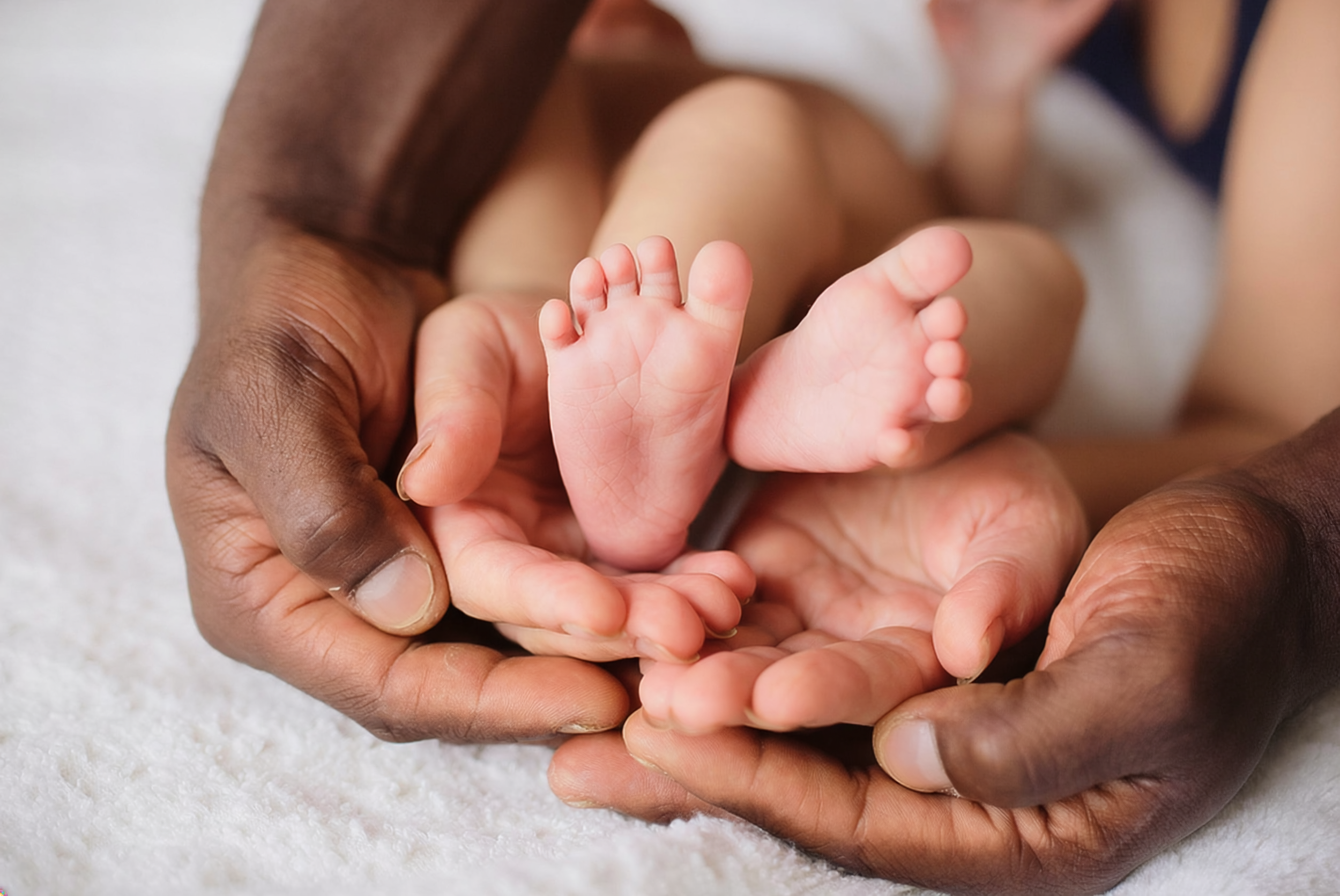 Close-up of a newborn baby feet held gently by an adult's hands.
