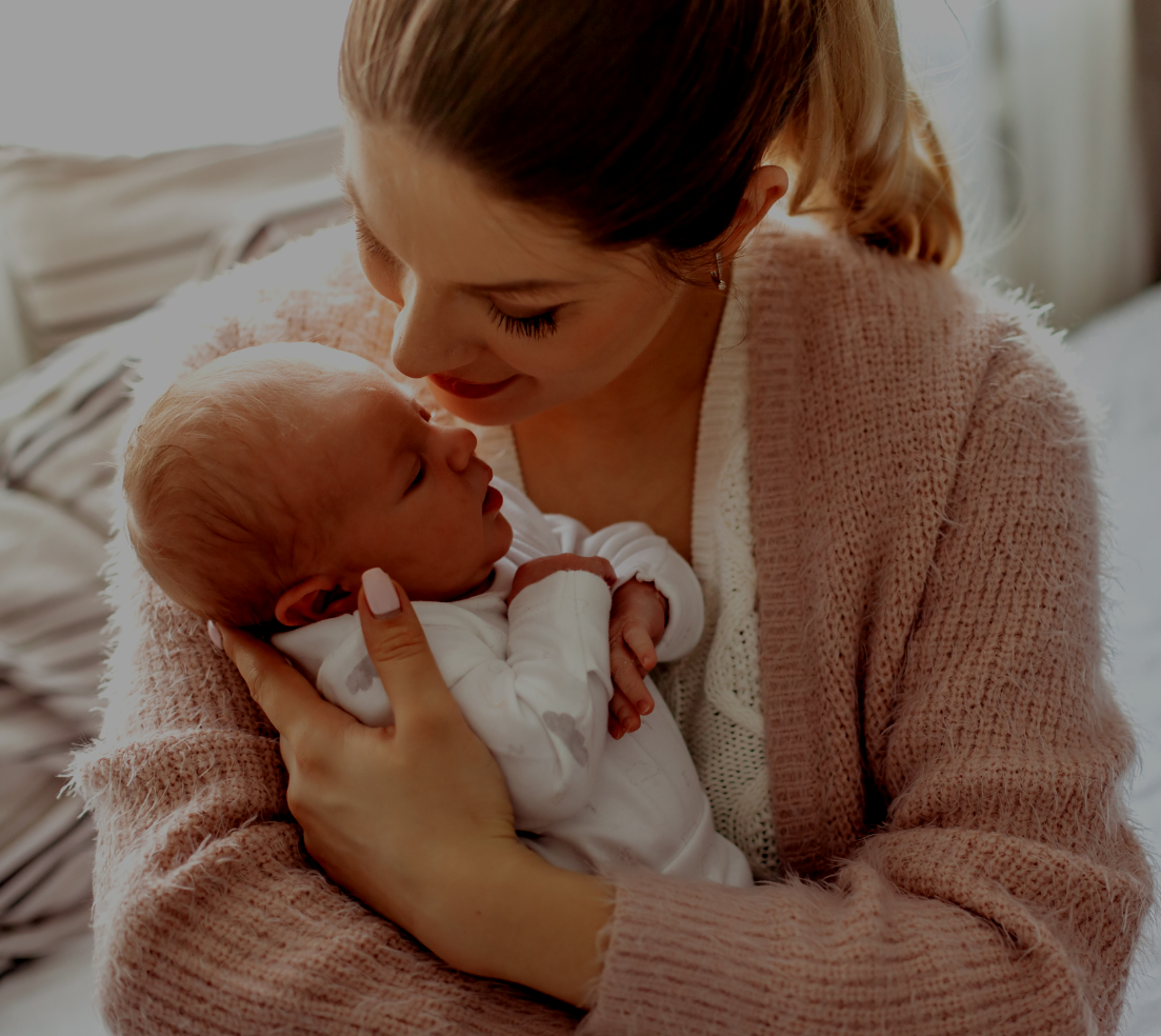 A woman holding a newborn baby close to her face, both gazing at each other affectionately indoors.